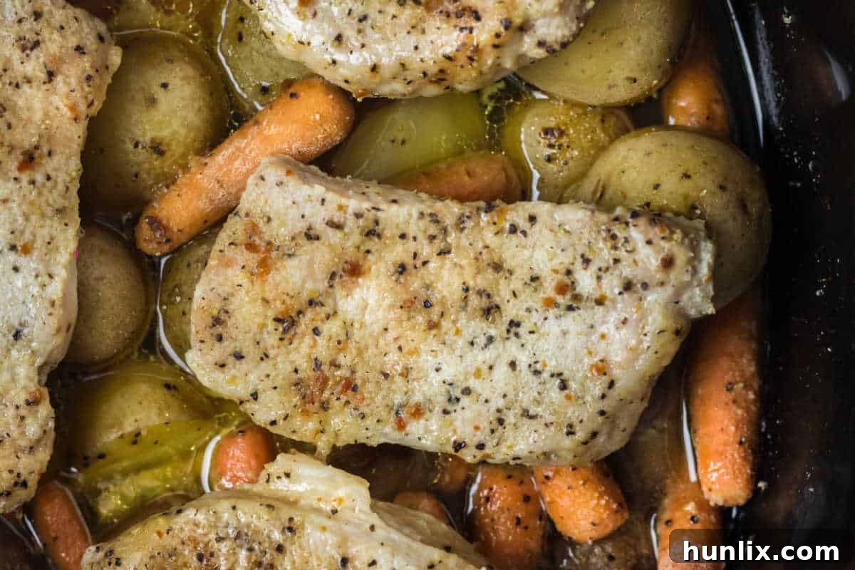 Overview shot of Italian pork chops and veggies cooking gently in a Crockpot, steaming with flavor.