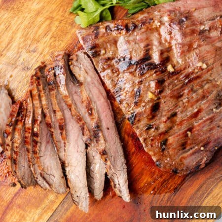 Grilled flank steak on a wooden cutting board with pieces sliced.
