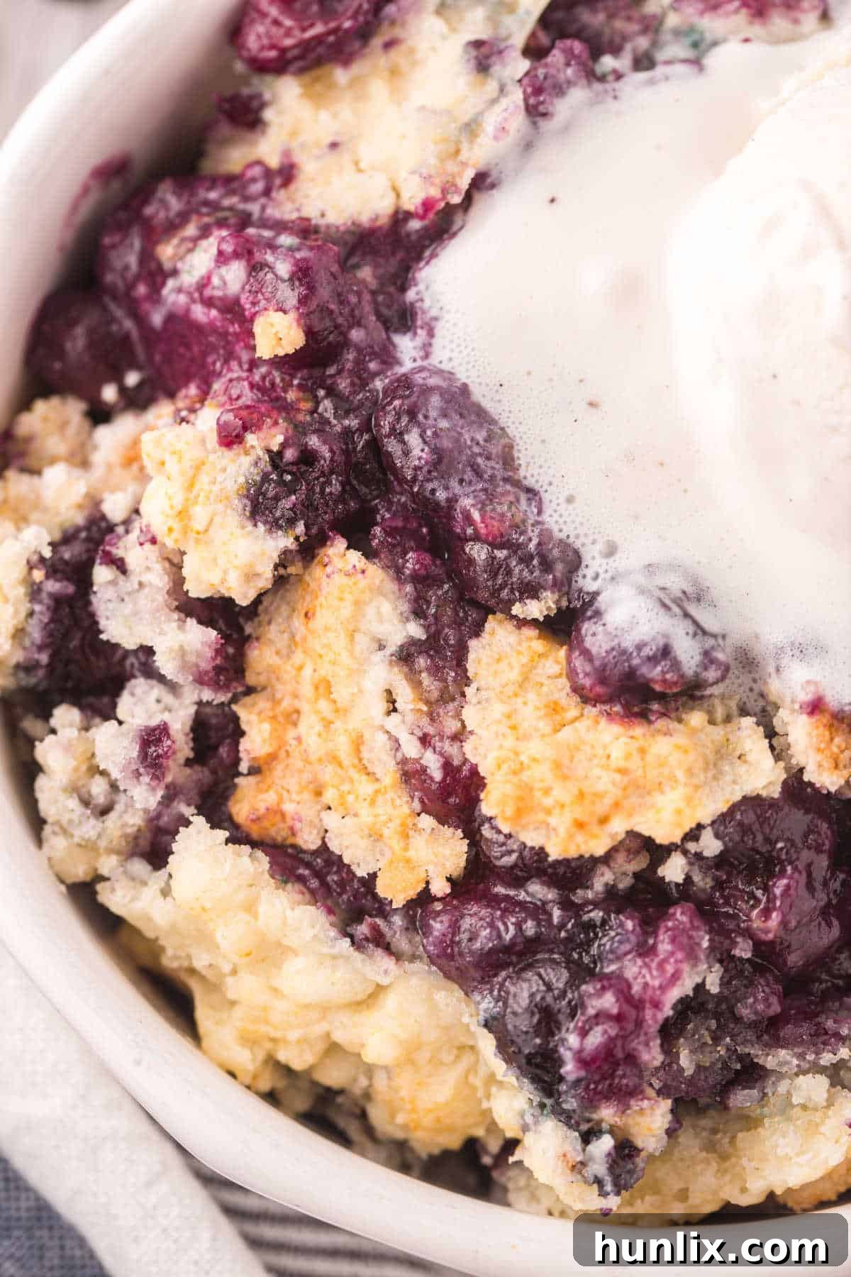 Bursting Blueberry Bliss 8 Blueberry cobbler in a bowl with melting vanilla ice cream.