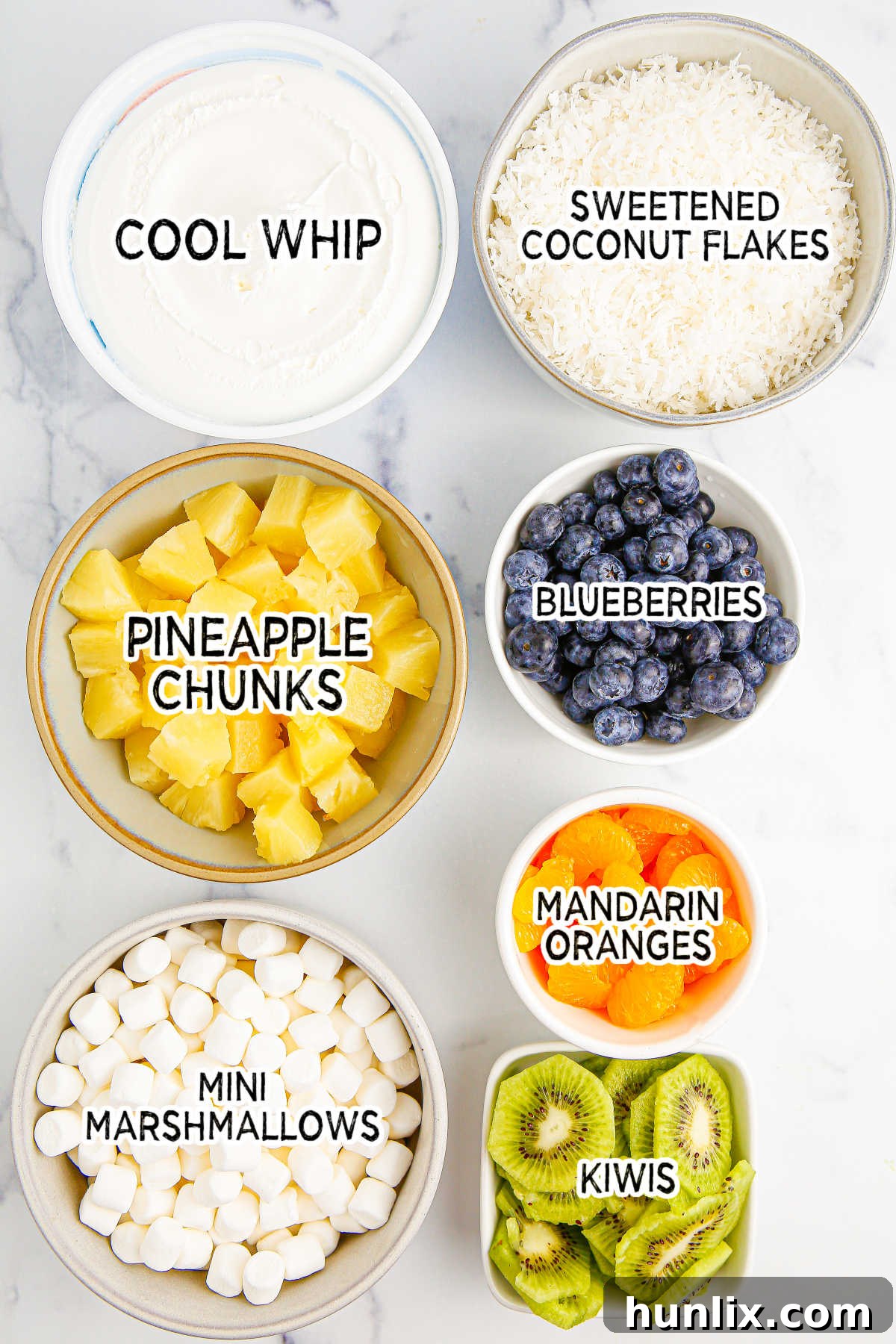 Tropical Cloud Delight 3 Various fresh and canned ingredients laid out for making tropical fluff salad, including Cool Whip, pineapple, mandarin oranges, blueberries, kiwis, marshmallows, and coconut flakes.