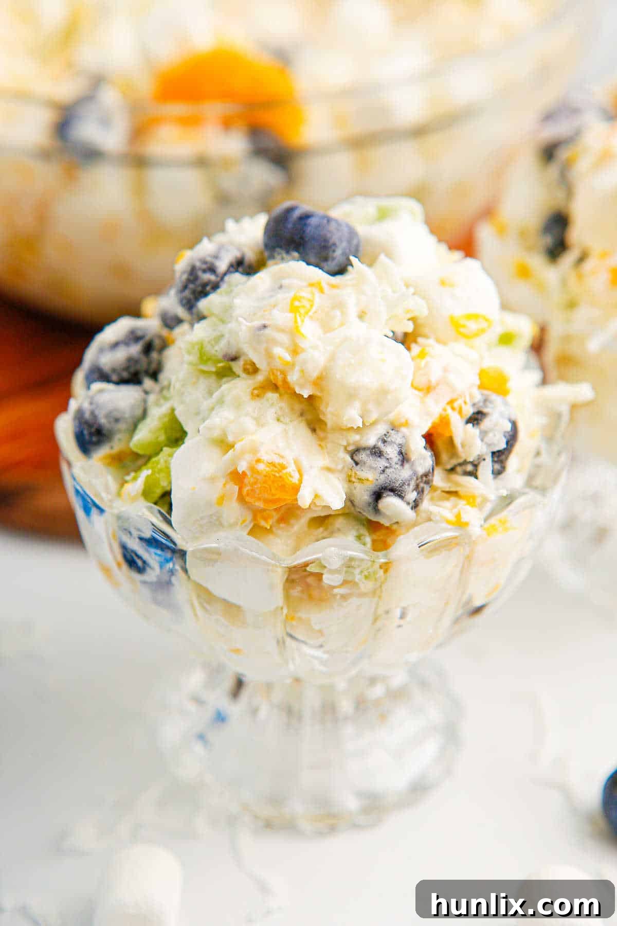 Tropical Cloud Delight 8 A parfait glass filled with Tropical Fluff Salad, highlighting its layers and presentation, ready for individual serving at an event.