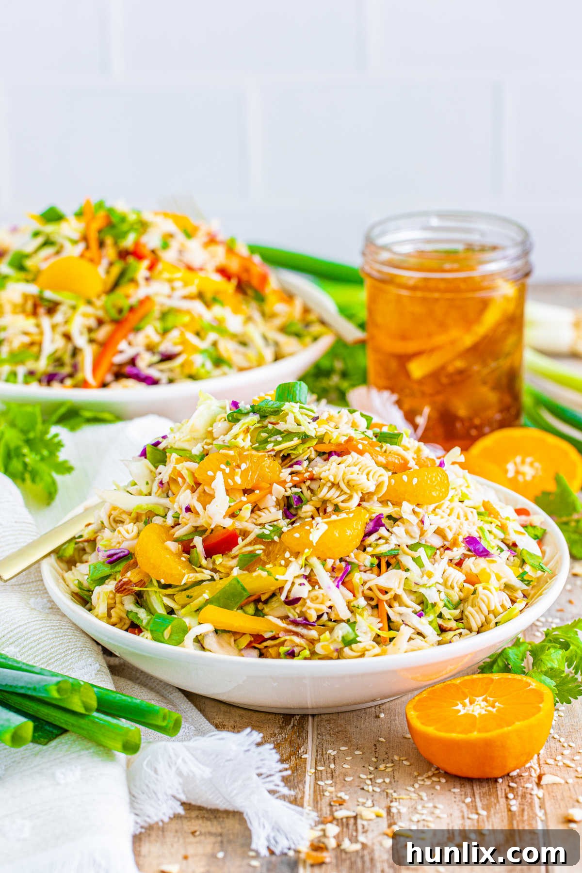 A vibrant ramen noodle salad on a white plate, garnished with sesame seeds.