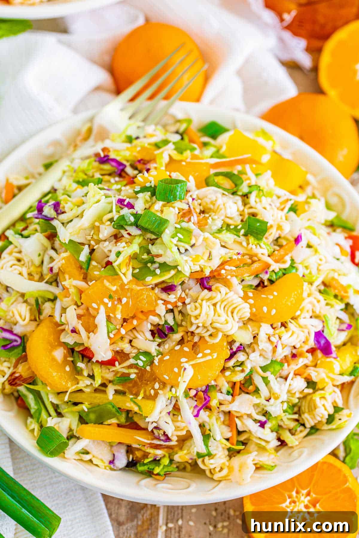 A fork taking a bite of ramen noodle salad from a white plate.