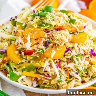 A ramen noodle salad on a white plate with a fork poised to take a bite.