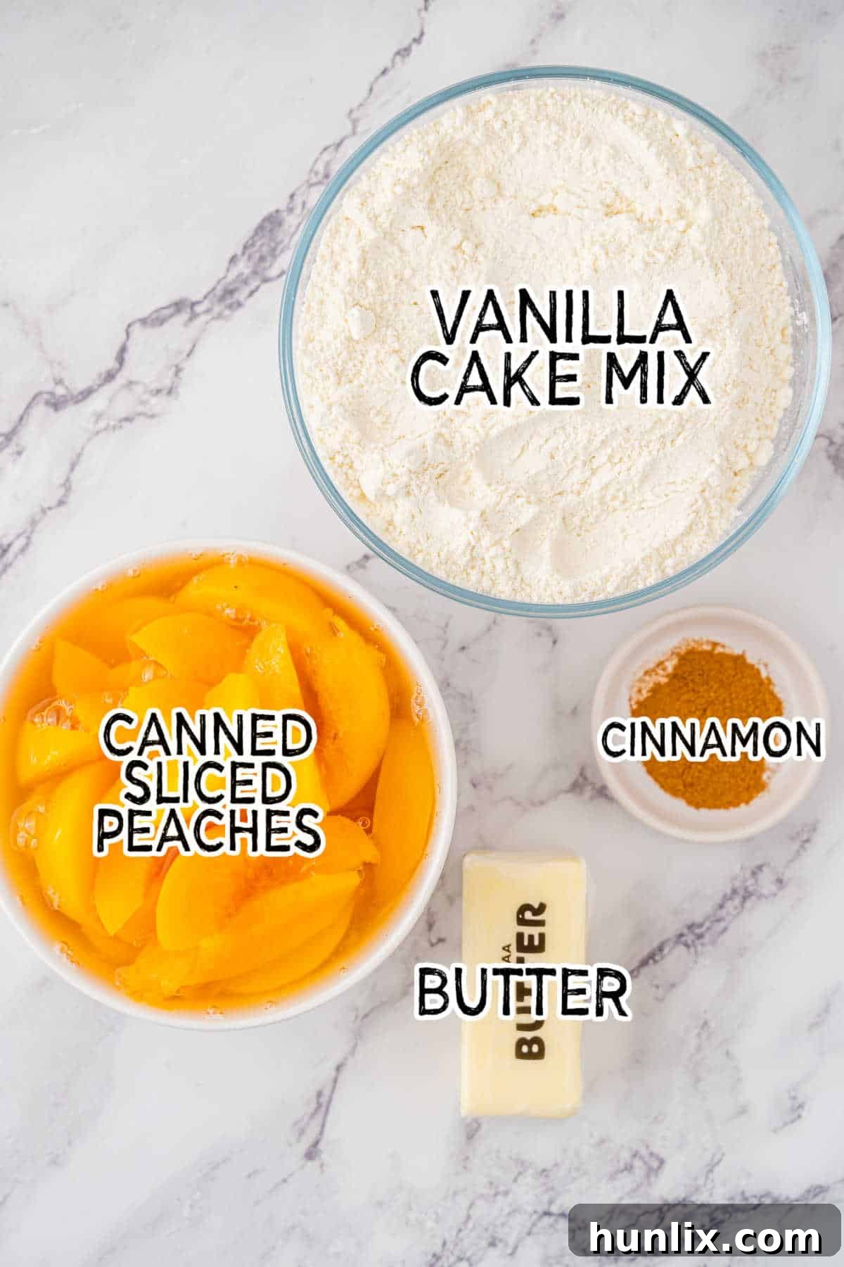 Effortless Peach Cobbler Cake 3 Fresh peaches, a box of vanilla cake mix, a stick of butter, and a container of cinnamon spice on a white marble countertop.