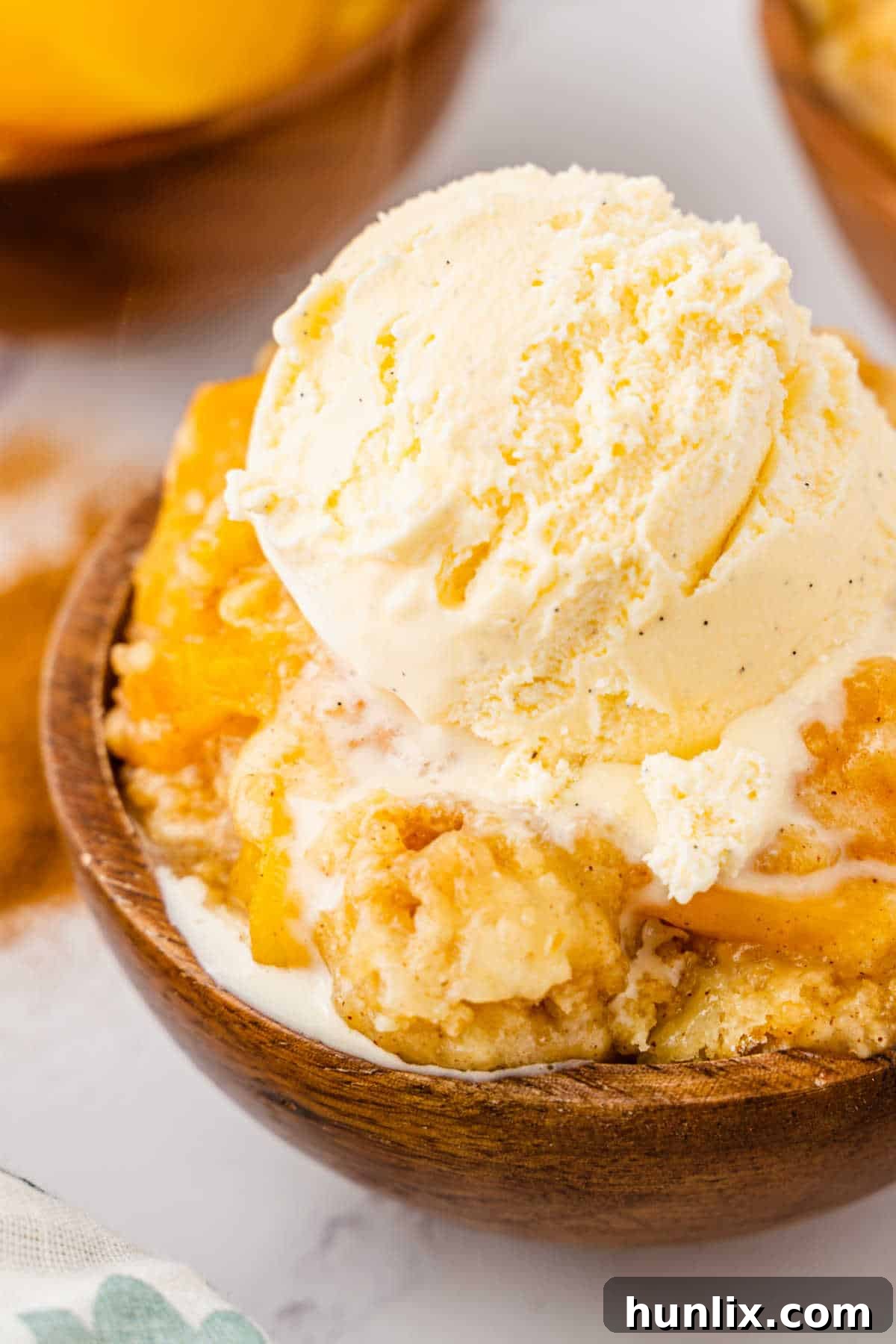 Effortless Peach Cobbler Cake 5 A single serving of peach cobbler dump cake in a white bowl, topped with a generous scoop of vanilla ice cream, ready to be enjoyed.