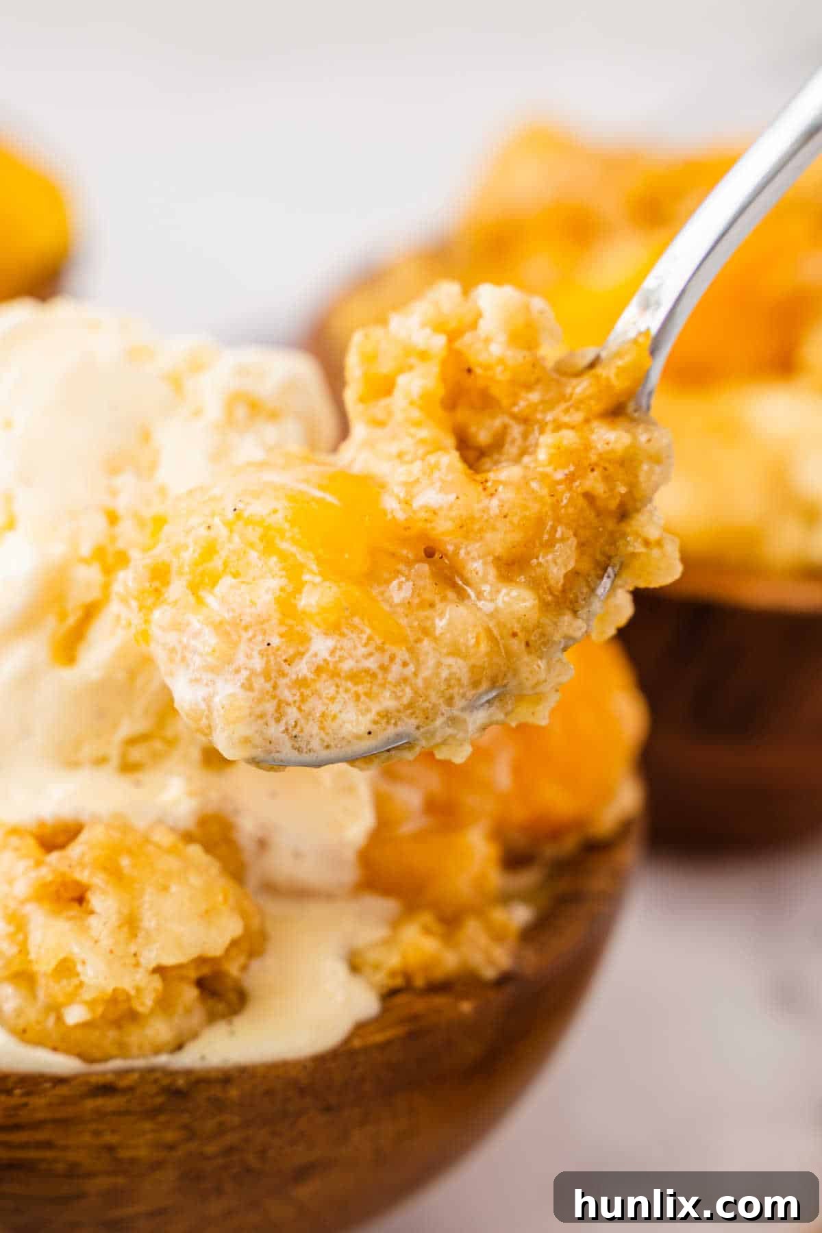 Effortless Peach Cobbler Cake 6 A close-up shot of peach cobbler dump cake on a spoon, showing the tender peaches and the golden, crumbly cake topping.