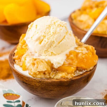 Effortless Peach Cobbler Cake 8 The recipe in a wooden bowl topped with vanilla ice cream.