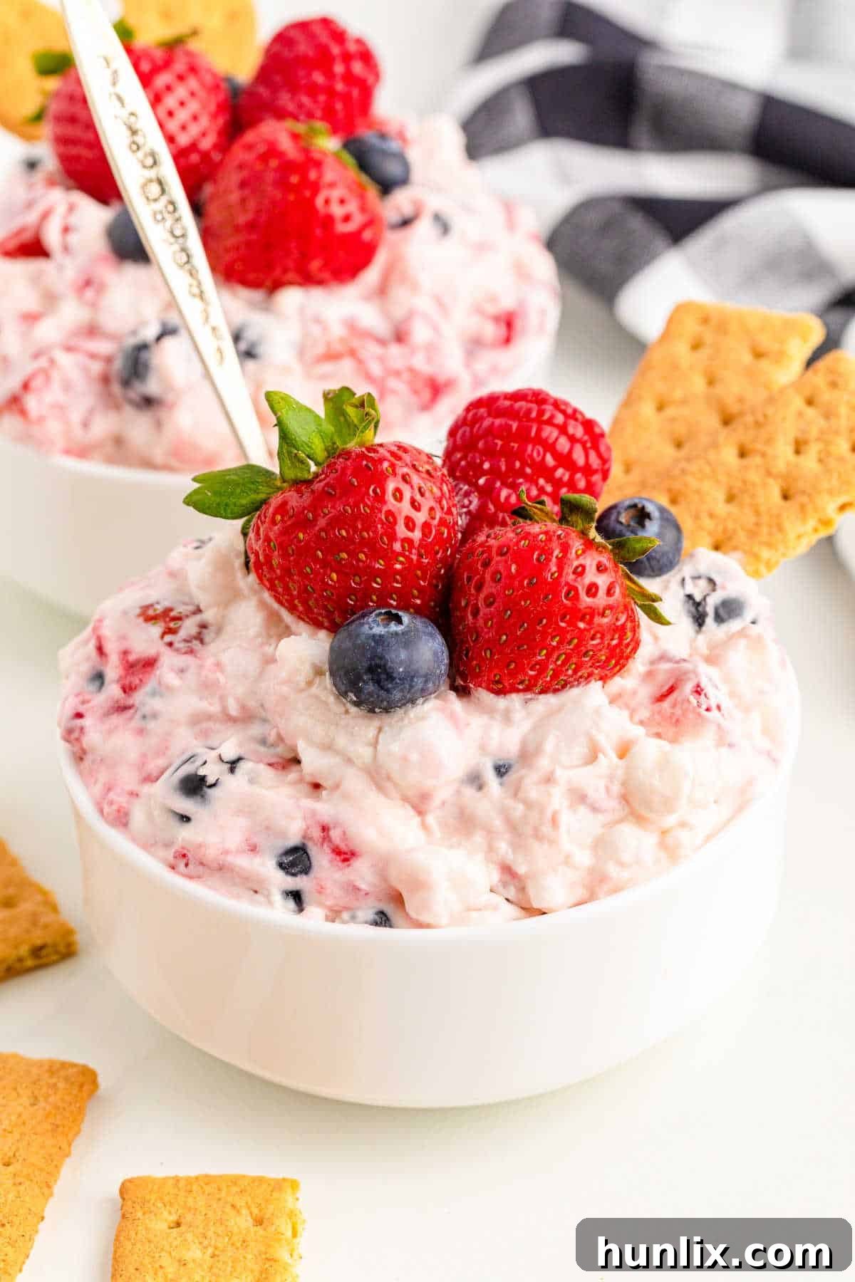 A glistening bowl of Berry Cheesecake Fluff, adorned with an assortment of fresh red and blue berries, ready to be served with a spoon.