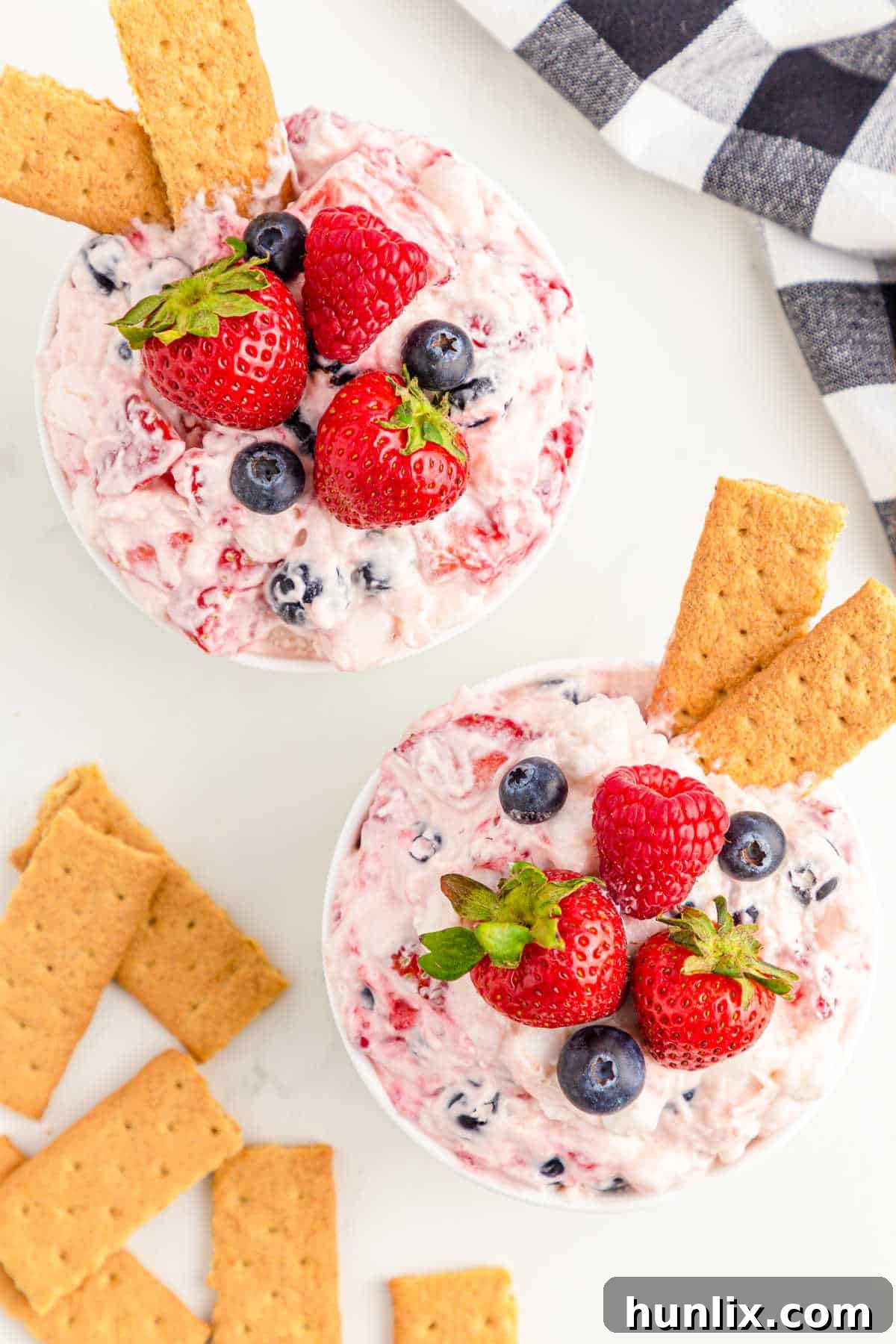 Two individual bowls of Berry Cheesecake Fluff, garnished with graham crackers, highlighting the creamy texture and fresh berries.