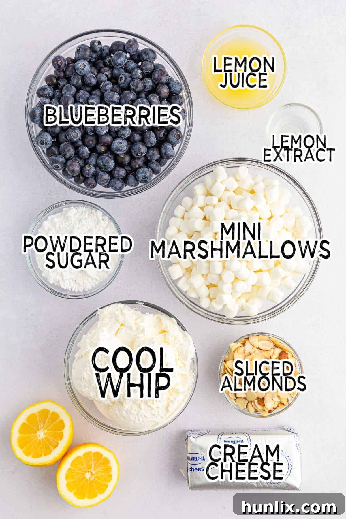 A collection of ingredients laid out, including cream cheese, powdered sugar, Cool Whip, lemons, blueberries, and marshmallows, ready to make Lemon Blueberry Fluff.