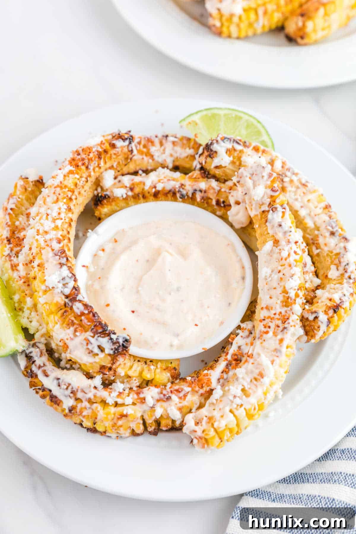 Air fryer corn ribs served on a white plate with a side of creamy dip, garnished with fresh herbs.