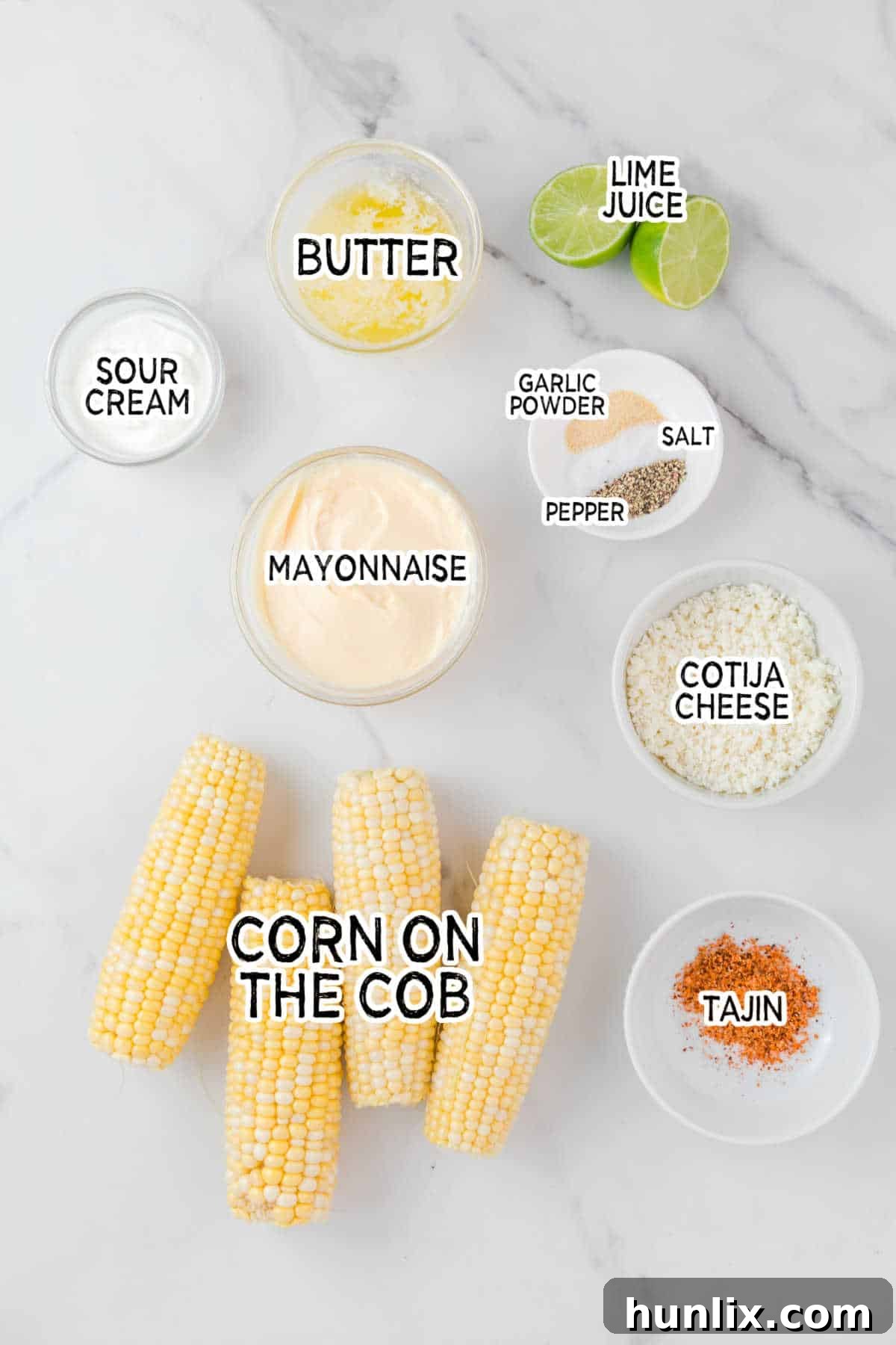 Ingredients for air fryer corn ribs laid out on a white marble counter, including corn cobs, butter, mayonnaise, and spices.