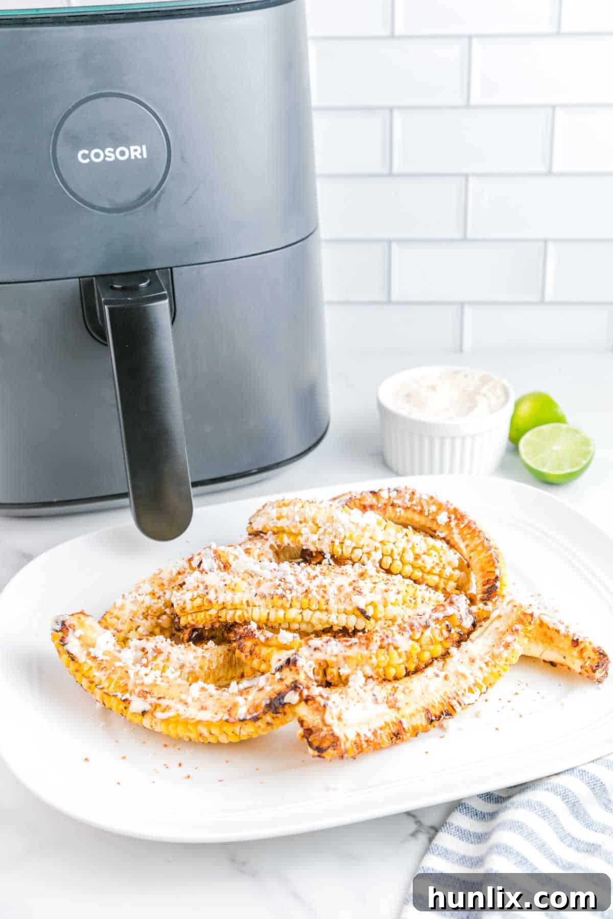 Air fryer corn ribs served on a platter, garnished with cheese and lime wedges.