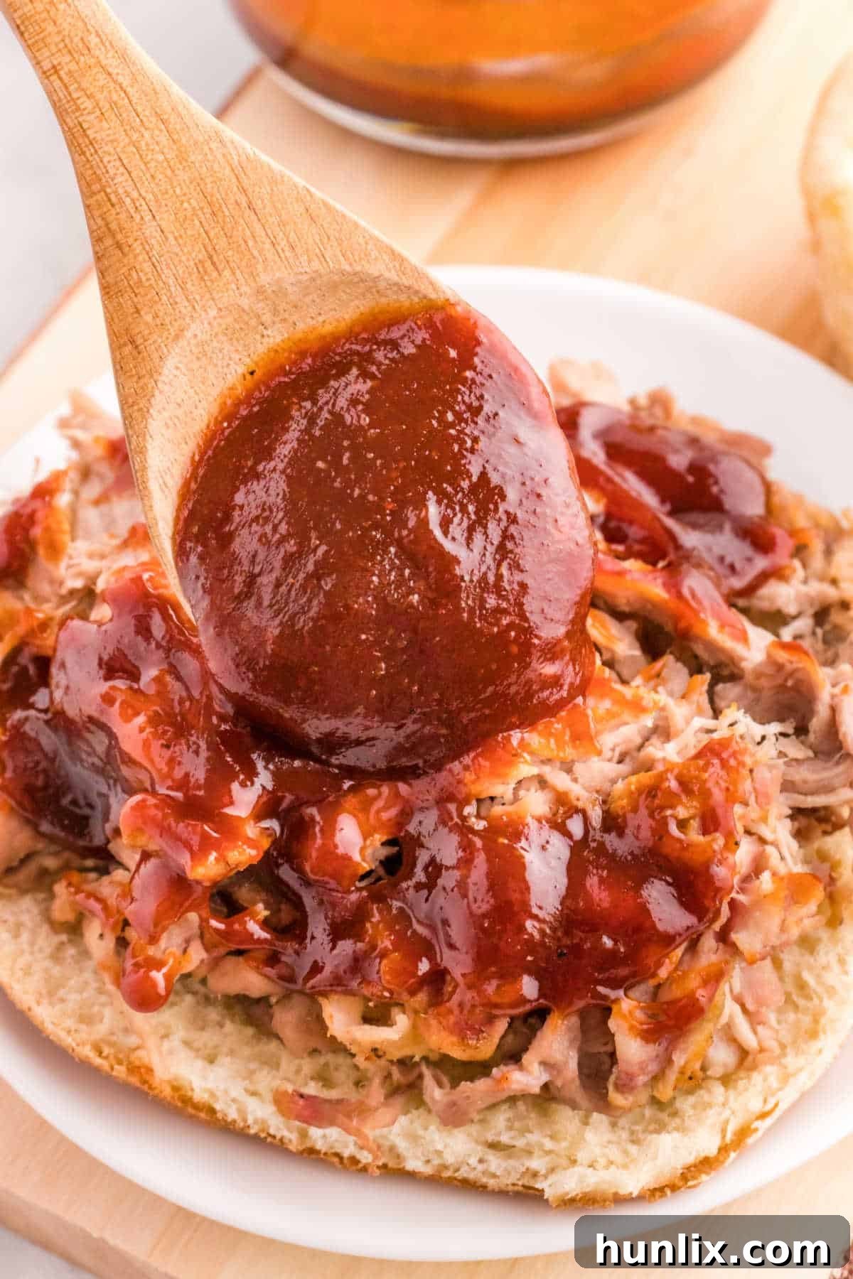 Signature Homemade BBQ Sauce 6 A wooden spoon putting bbq sauce on chicken on a bun.