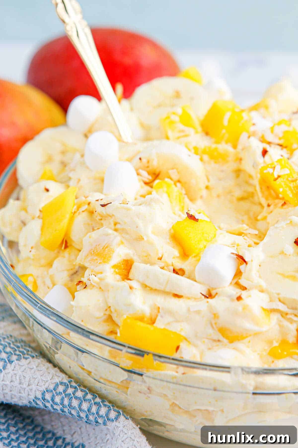 Tropical Mango Banana Fluff 8 A bowl of mango banana marshmallow salad with a serving spoon, highlighting its creamy texture and fresh fruit pieces.