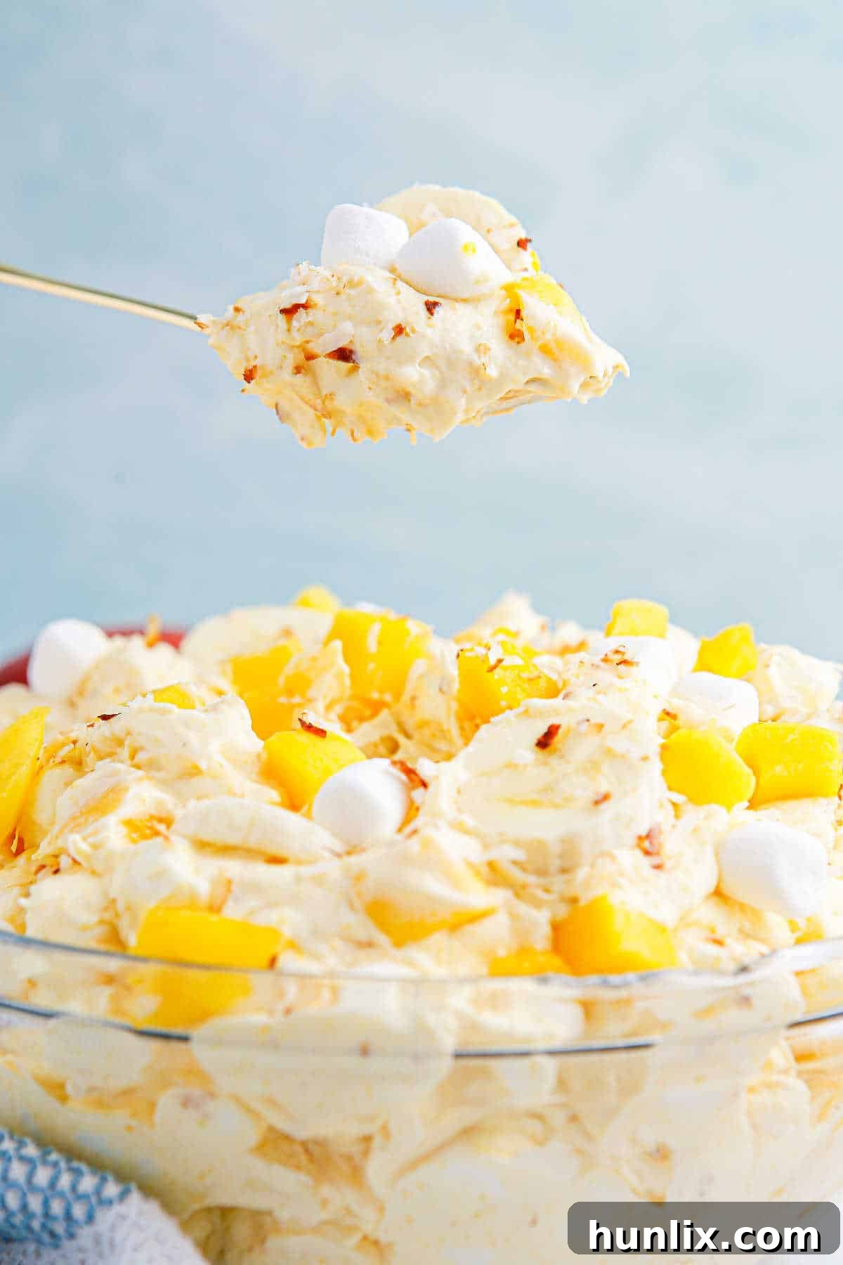 Tropical Mango Banana Fluff 9 A serving spoon lifting a portion of mango banana marshmallow salad over a bowl, showcasing its rich and appealing texture.