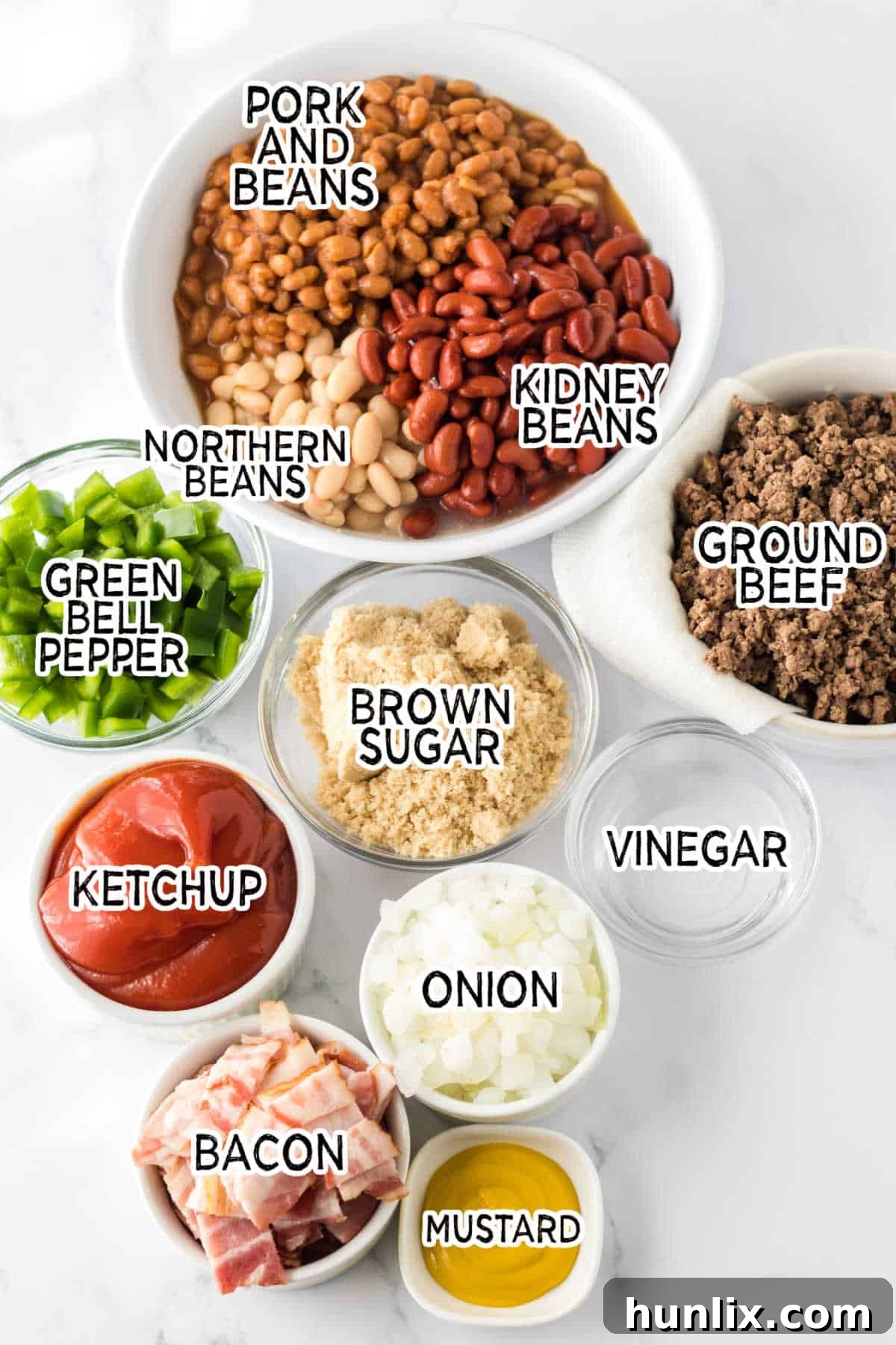 Various ingredients laid out on a wooden surface, including canned beans, ground beef, bacon, and vegetables, ready to be prepared for slow cooker cowboy beans.