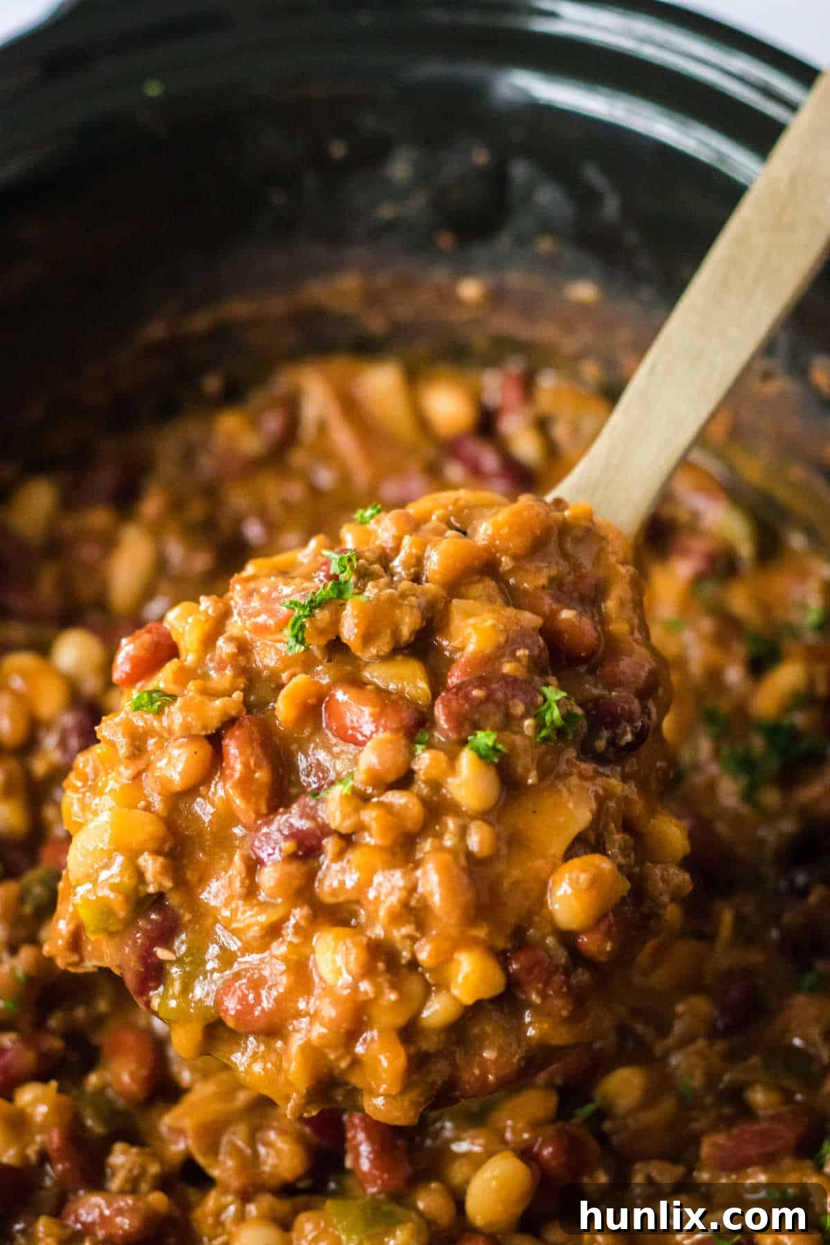 A close-up shot of slow cooker cowboy beans on a wooden spoon, showcasing their rich texture and hearty ingredients.