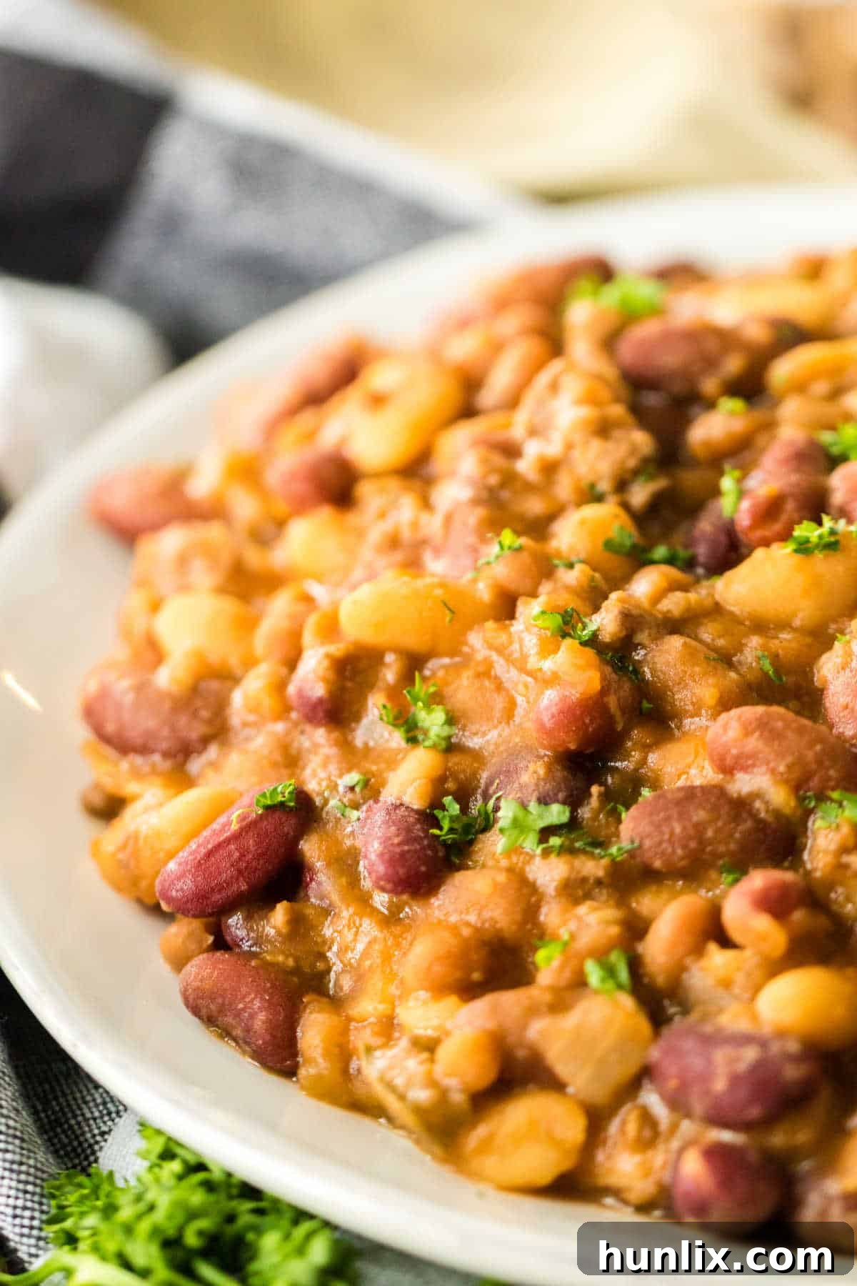 A close-up shot of slow cooker cowboy beans on a white plate, garnished with fresh herbs, ready to be enjoyed.