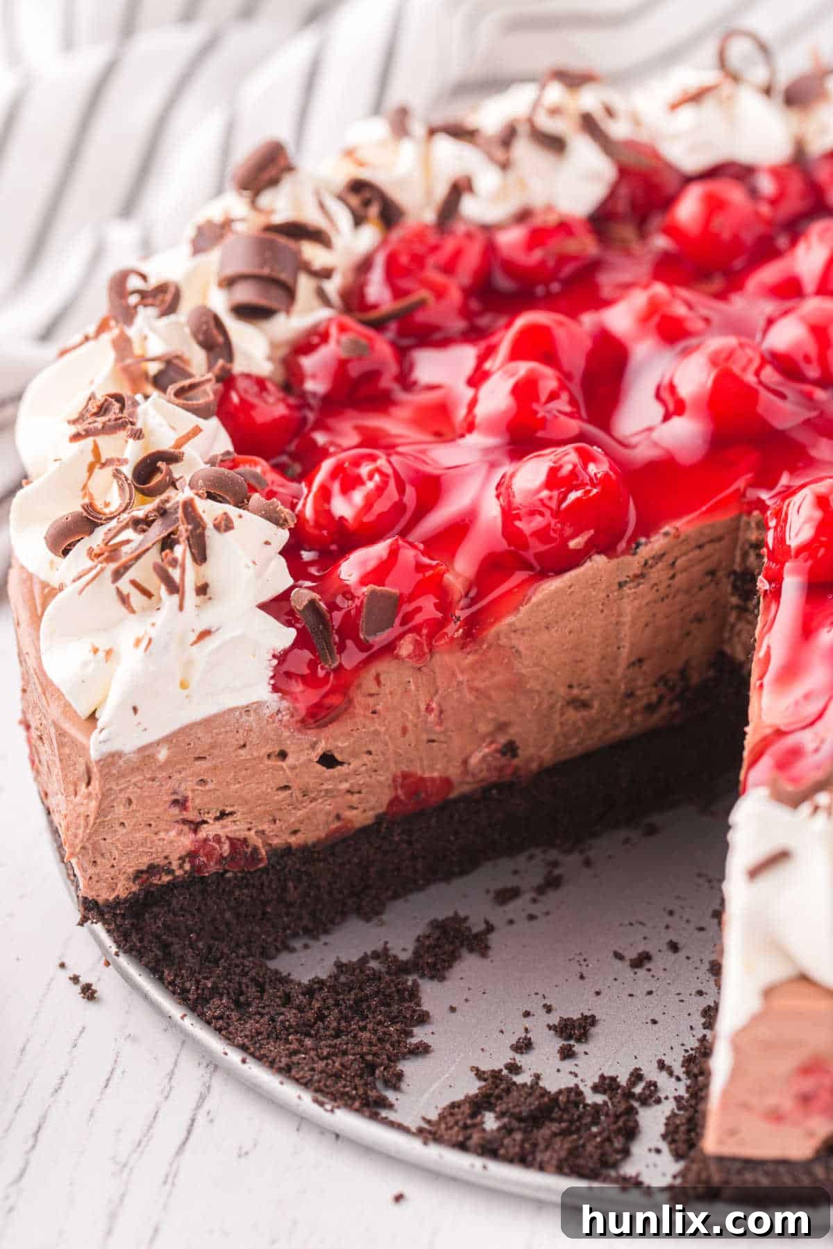 Black Forest Cheesecake with a slice removed, showcasing the creamy filling, Oreo crust, and cherry topping.