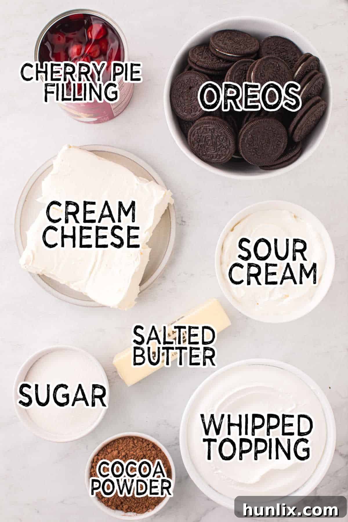 Various ingredients laid out to make black forest cheesecake, including Oreos, butter, cream cheese, cocoa powder, and cherry pie filling.