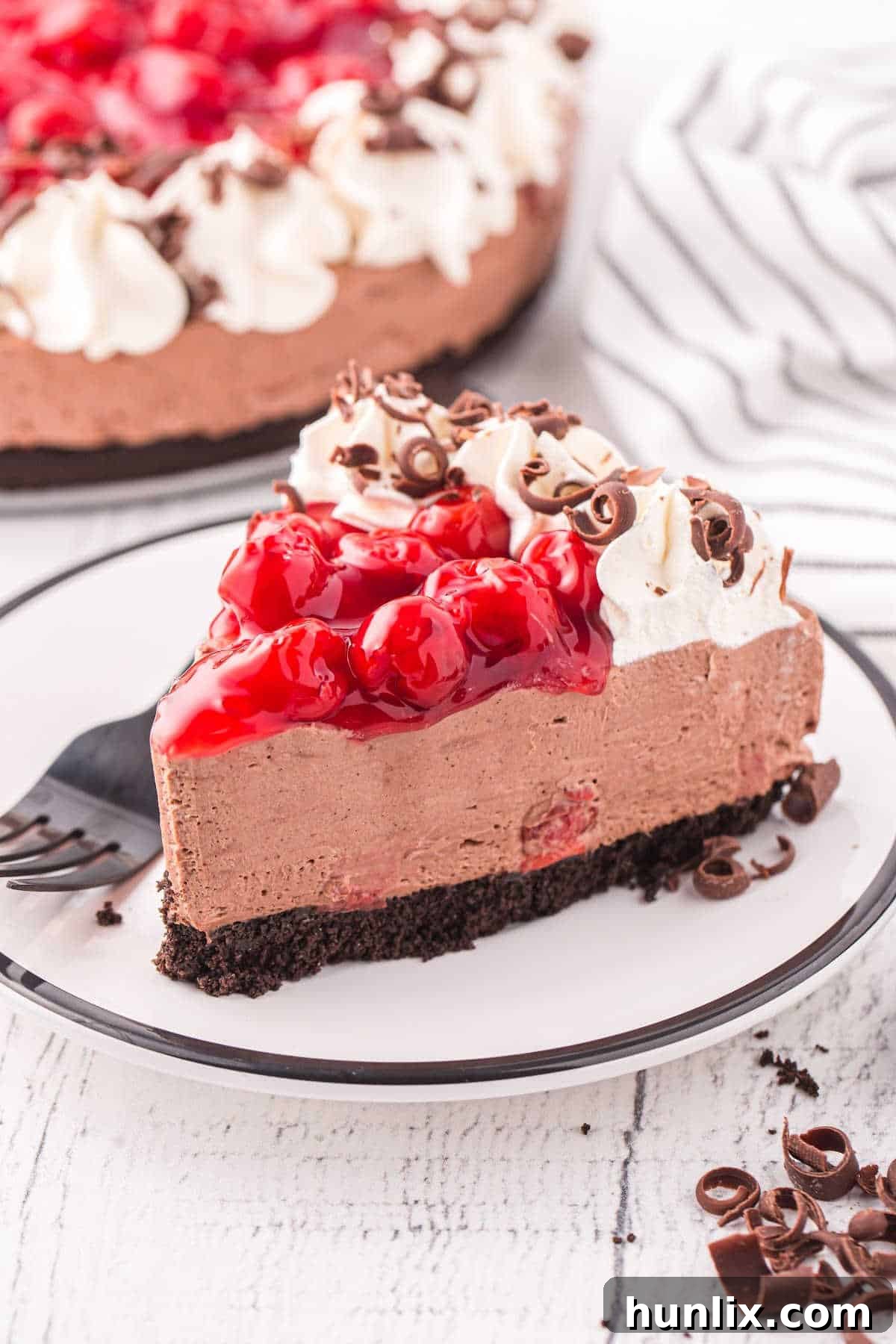 A slice of black forest cheesecake on a plate with a black fork, showing the distinct layers.