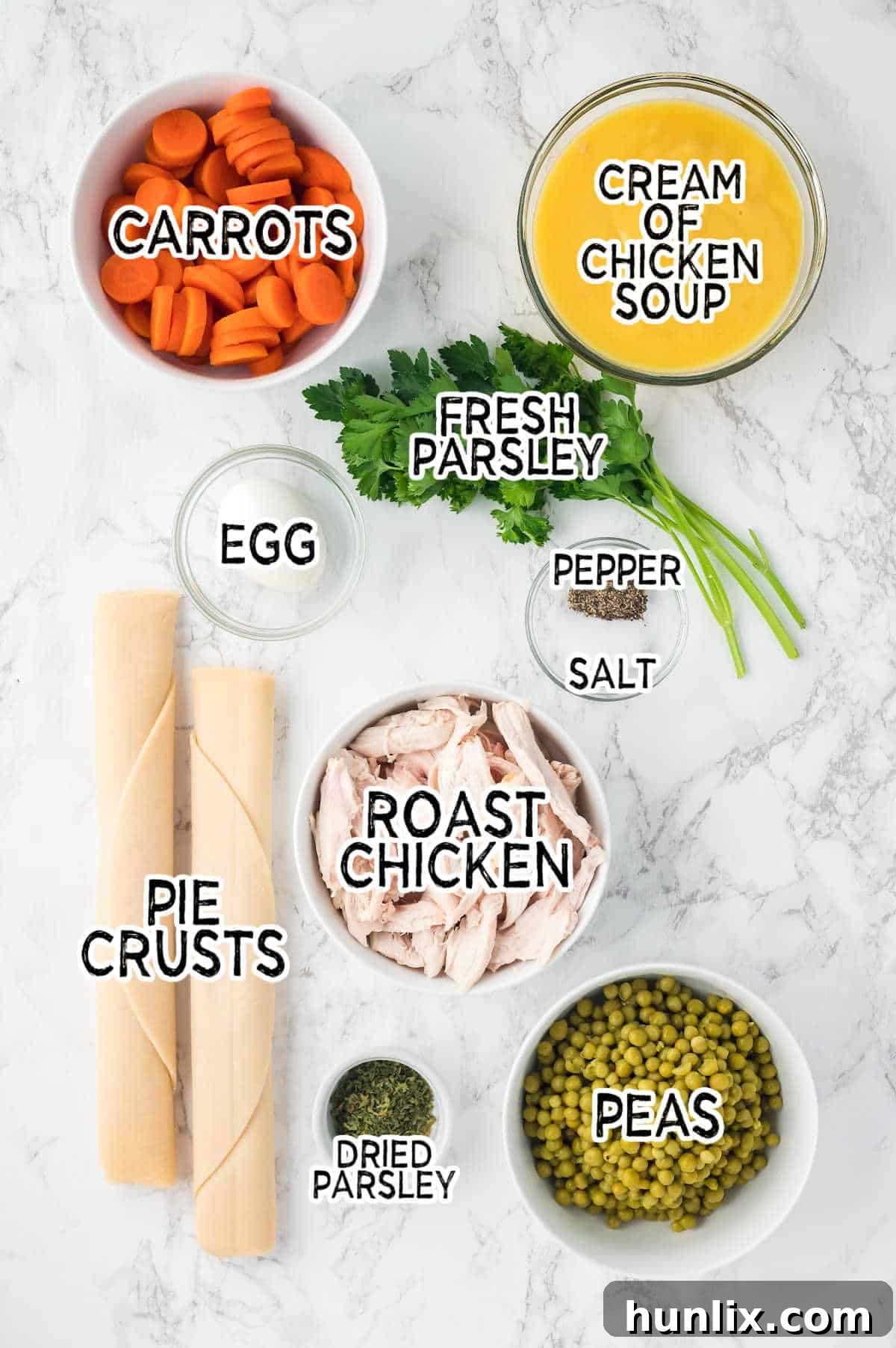 A collection of ingredients laid out on a table, including canned goods, chicken, spices, and pie crusts, ready to be combined for chicken pot pie.