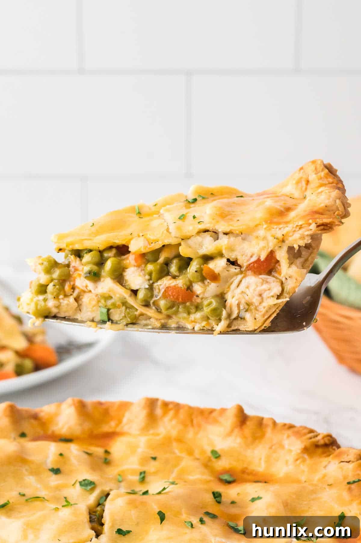 A pie server holding a generous slice of golden-brown chicken pot pie, ready to be placed on a plate.
