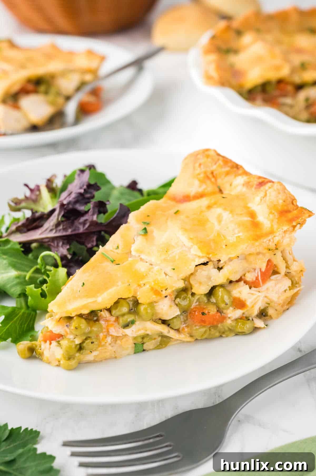 A slice of chicken pot pie served on a white plate, accompanied by a fresh green salad.