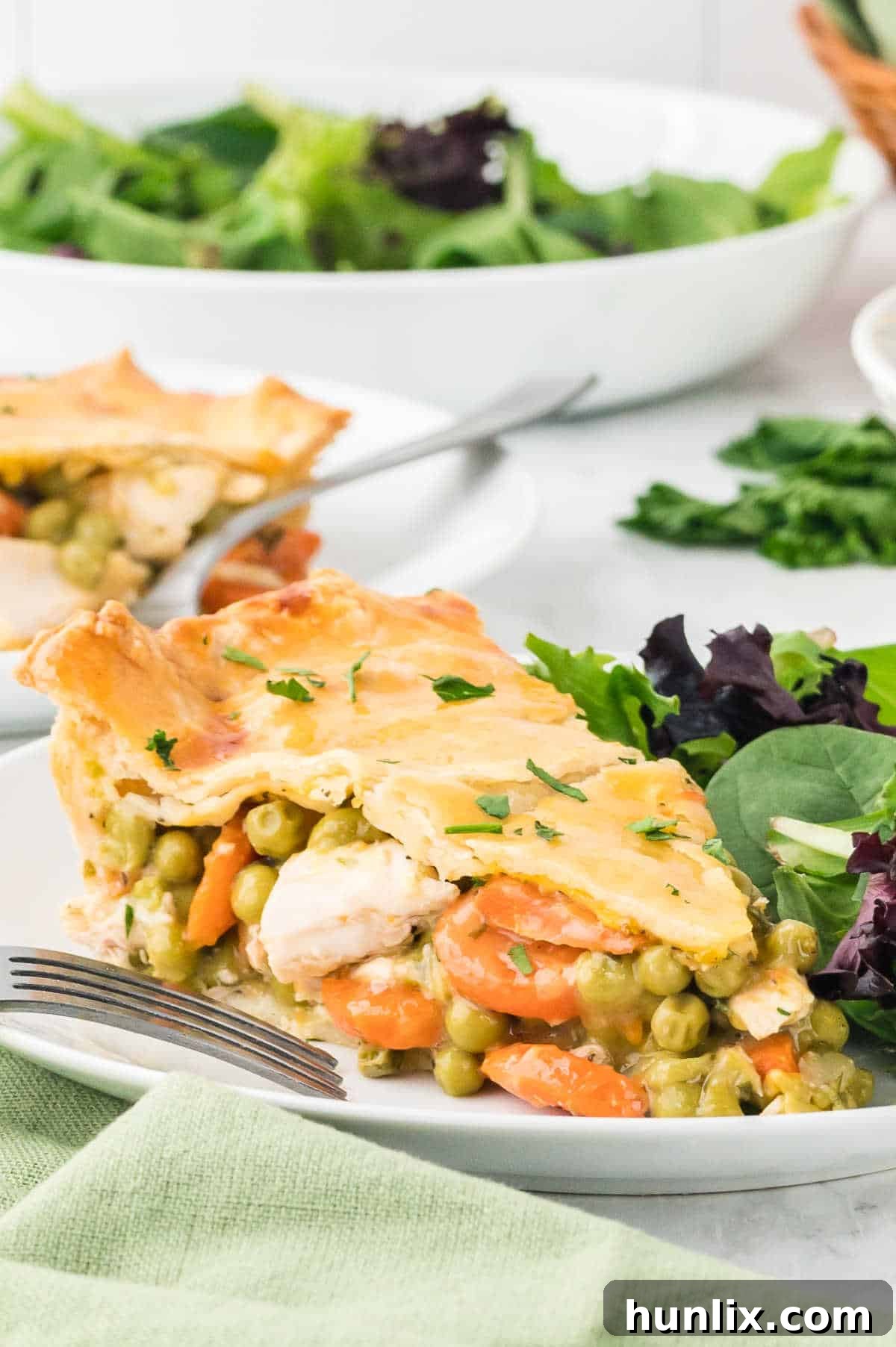Another enticing slice of chicken pot pie on a plate, alongside a fresh salad, highlighting its appeal.