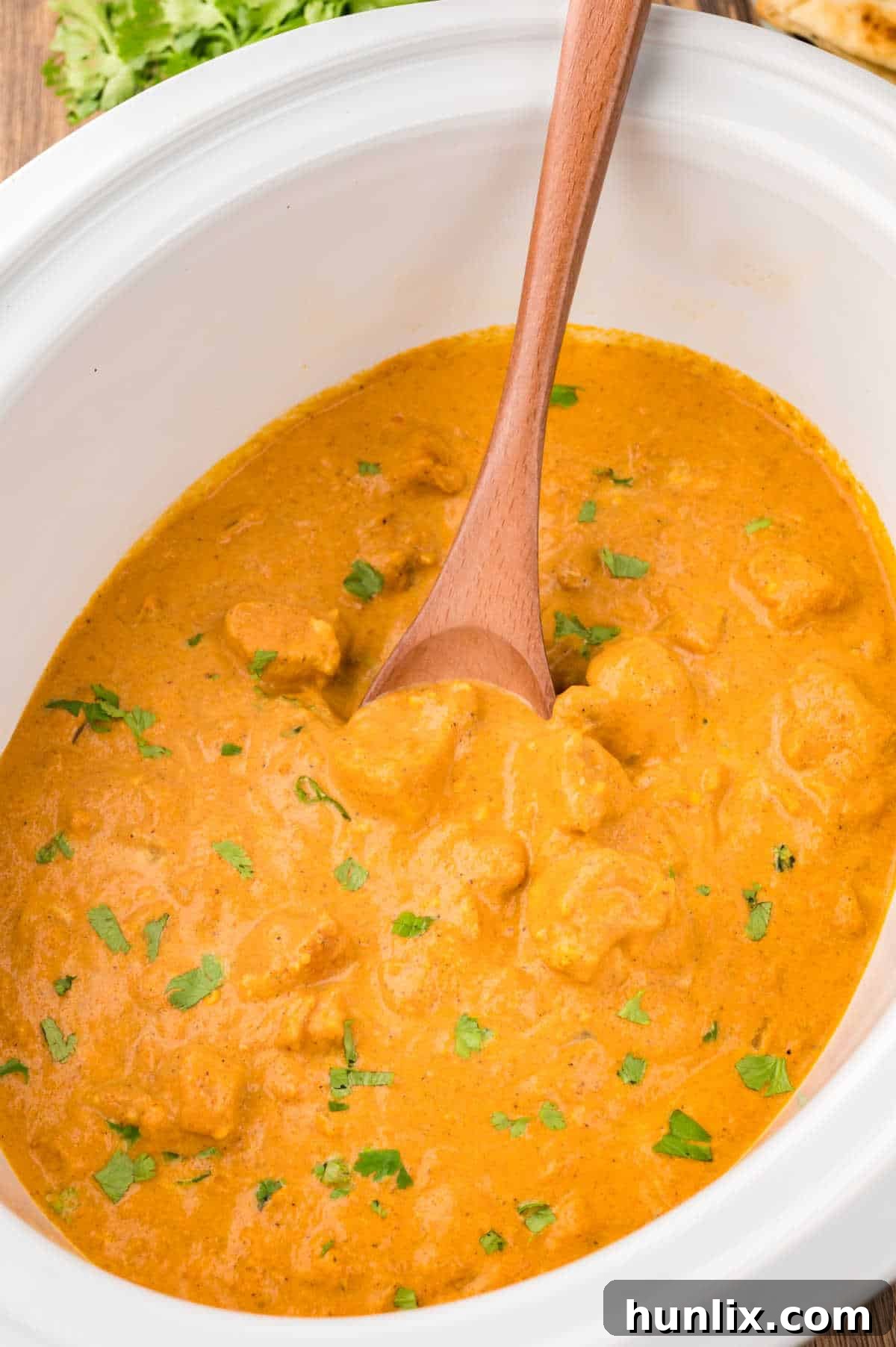Butter chicken in a slow cooker with a wooden spoon.