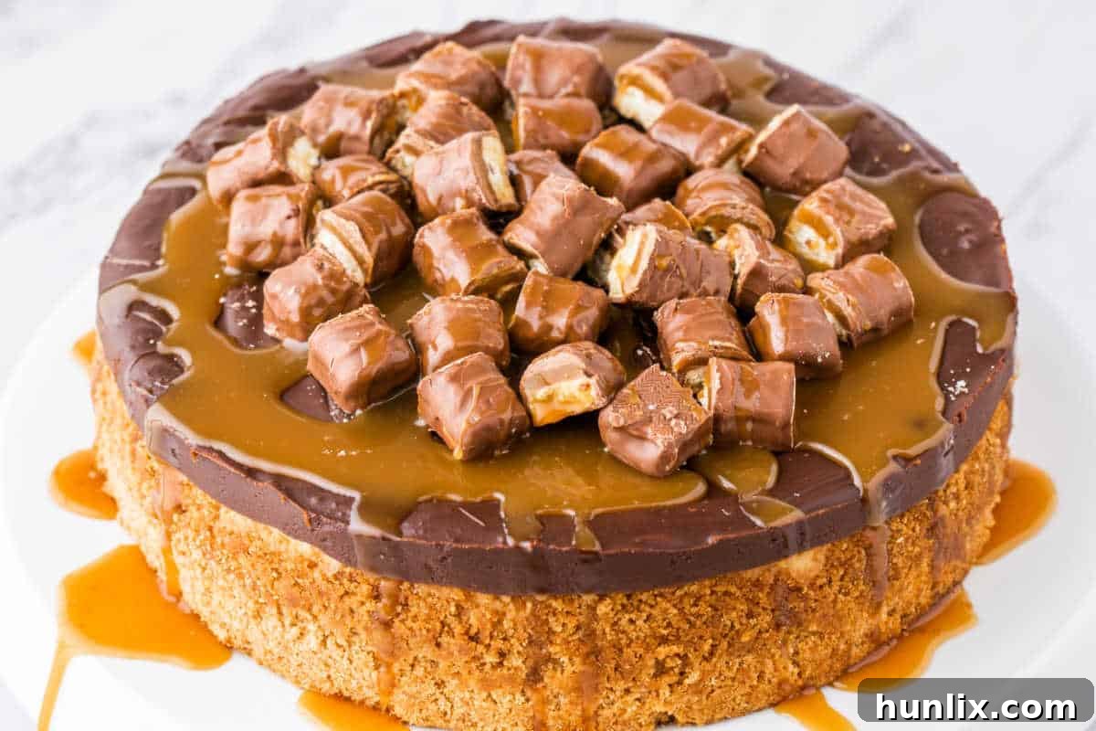 Twix Caramel Crunch Cheesecake 2 A beautifully crafted Twix Cheesecake on a white marble surface, ready to be sliced, garnished with Twix bars and caramel drizzle.