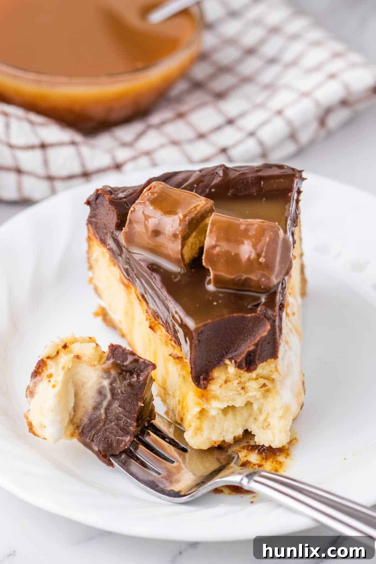 Twix Caramel Crunch Cheesecake 11 A delightful slice of Twix Cheesecake with a fork taking a bite, showcasing the perfect creamy texture and tempting layers of crust, filling, and chocolate ganache.
