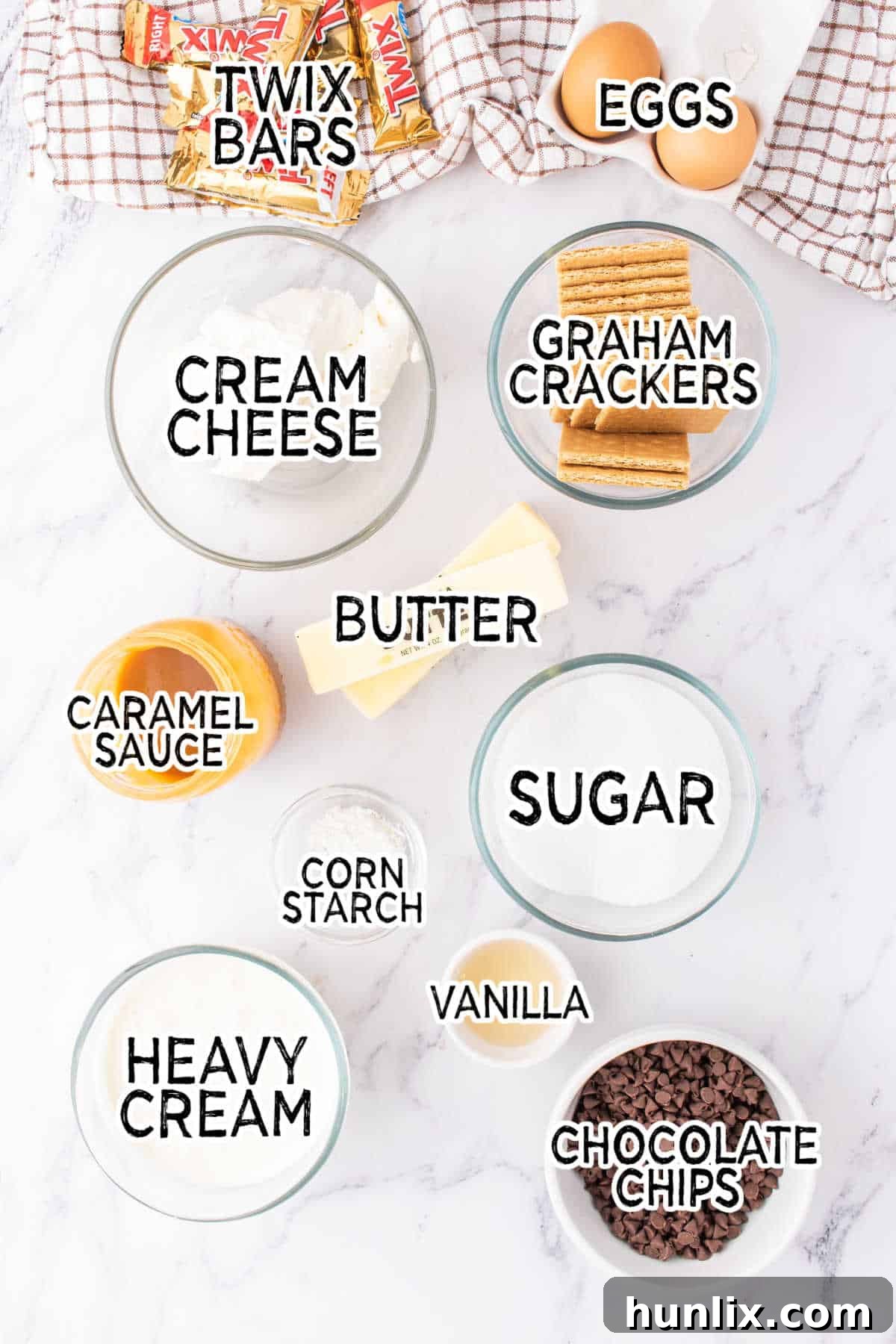 Twix Caramel Crunch Cheesecake 3 A selection of fresh ingredients laid out on a kitchen counter, including graham crackers, cream cheese, sugar, butter, and chocolate, all ready to be used to make the delicious Twix Cheesecake.