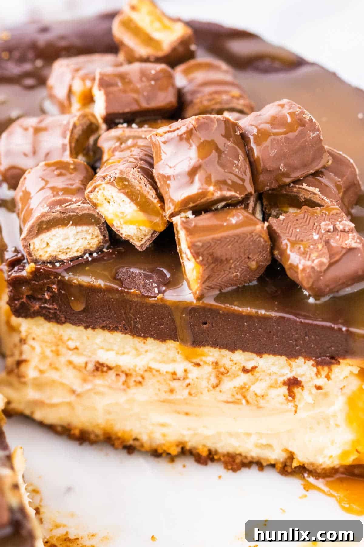 Twix Caramel Crunch Cheesecake 9 A perfectly sliced piece of Twix Cheesecake on a white plate, showcasing the distinct layers of the golden crust, creamy caramel-infused filling, and rich chocolate ganache.