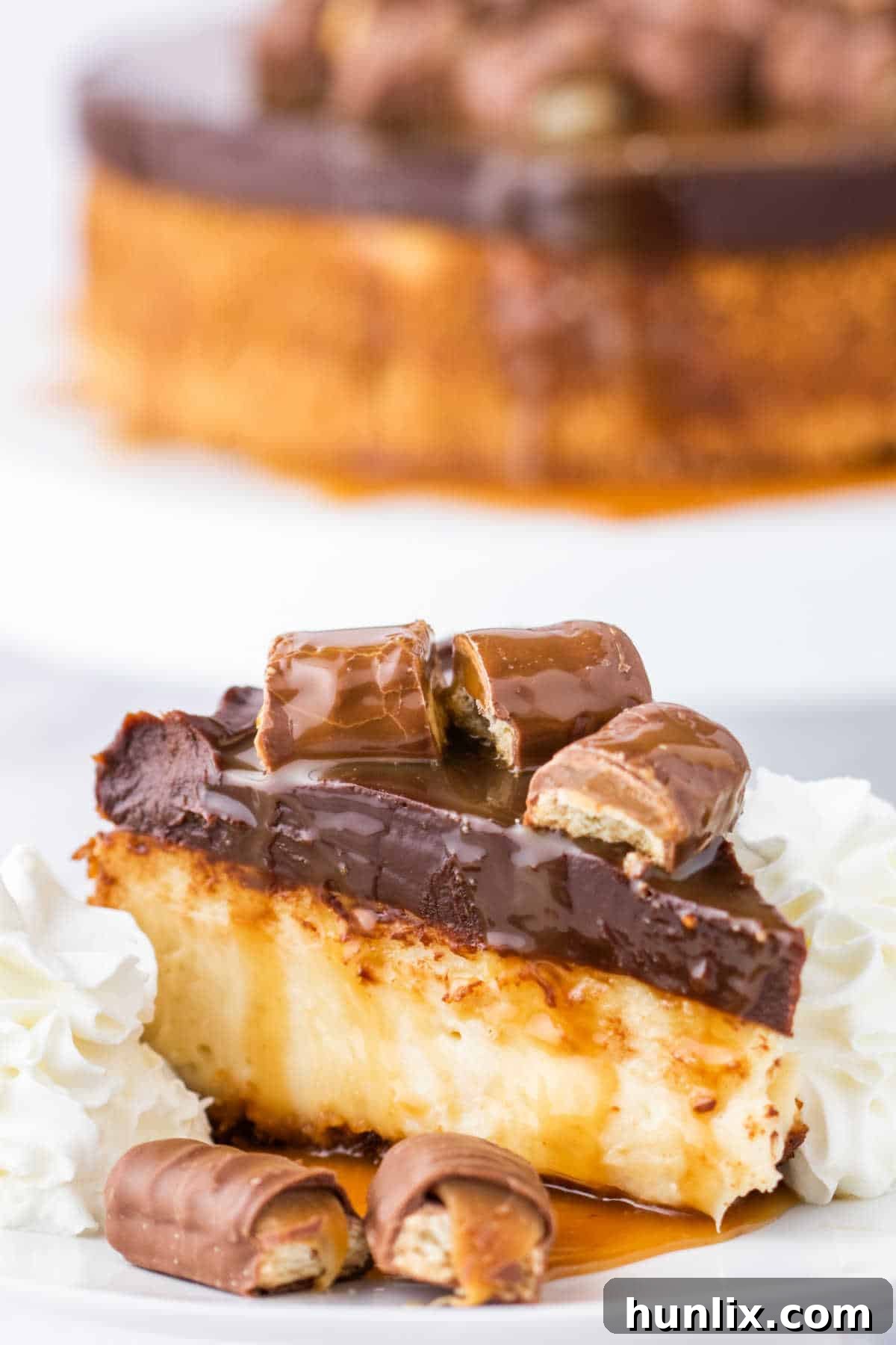 Twix Caramel Crunch Cheesecake 10 A single slice of Twix Cheesecake, beautifully plated and ready to be enjoyed, highlighting its rich texture and appealing layers, garnished with a piece of Twix.