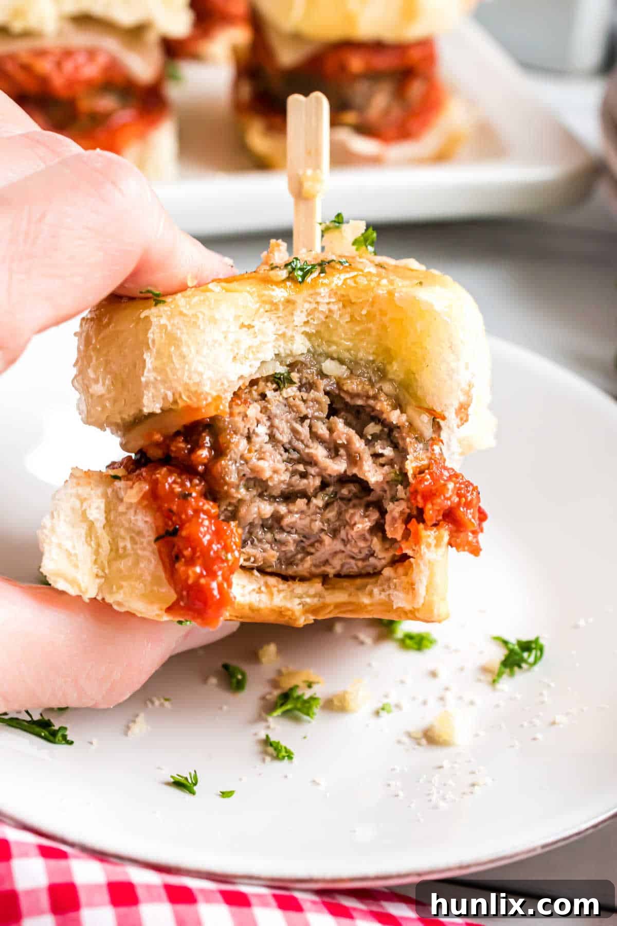 A hand holding a meatball slider with a bite taken out, showing the melted cheese and meatball.