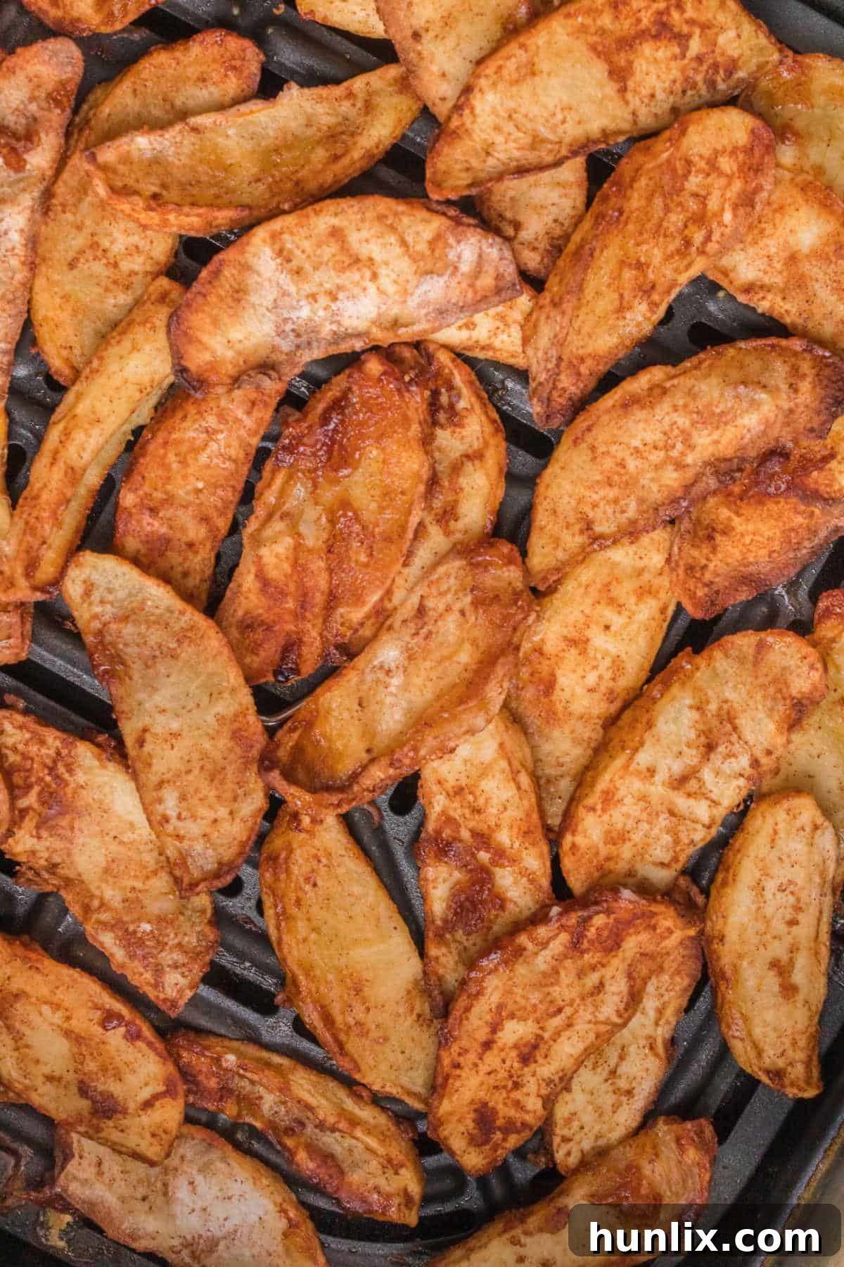 The recipe in an air fryer basket, showing golden brown apple slices.