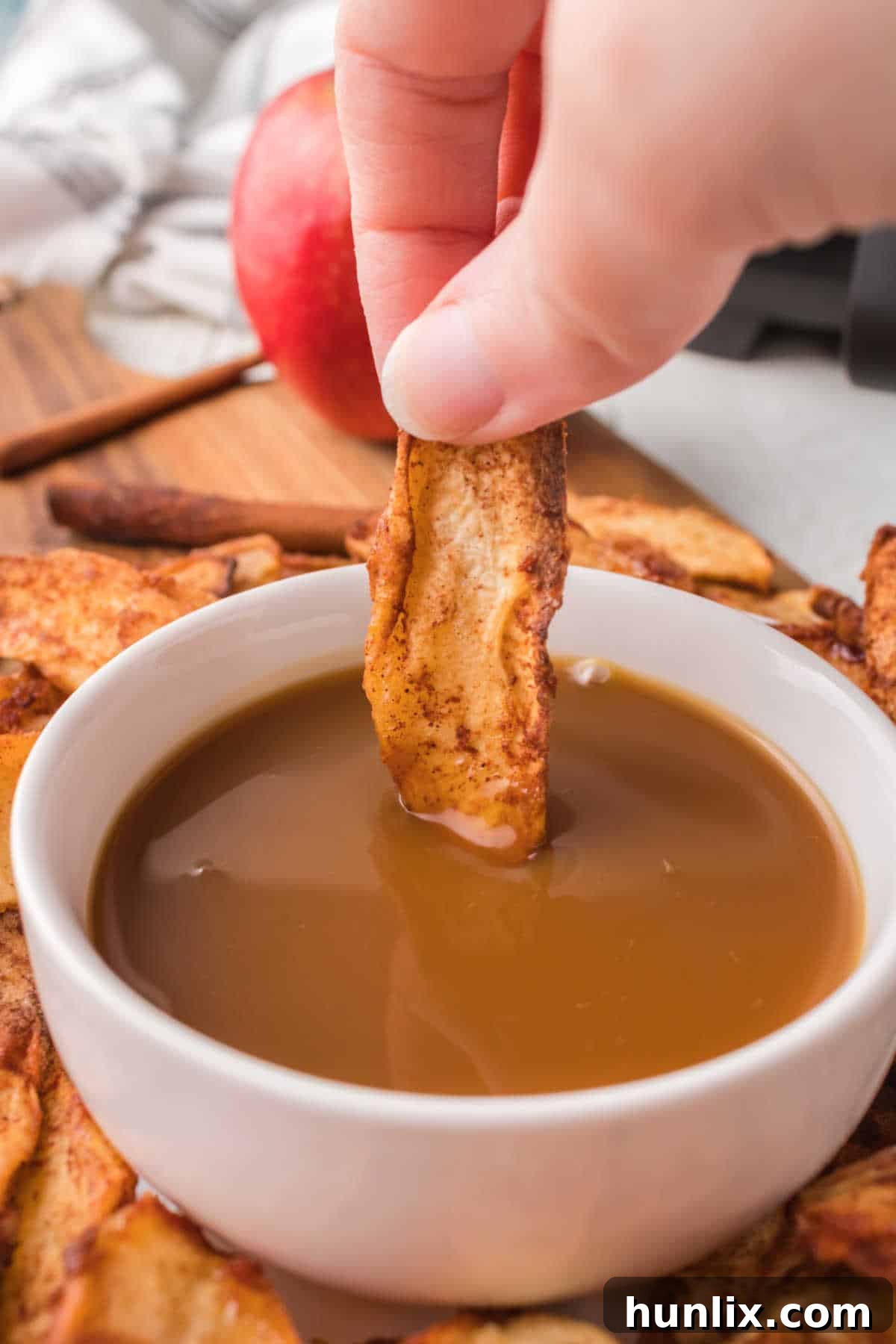 An air-fried apple slice being dipped into a bowl of creamy caramel sauce.