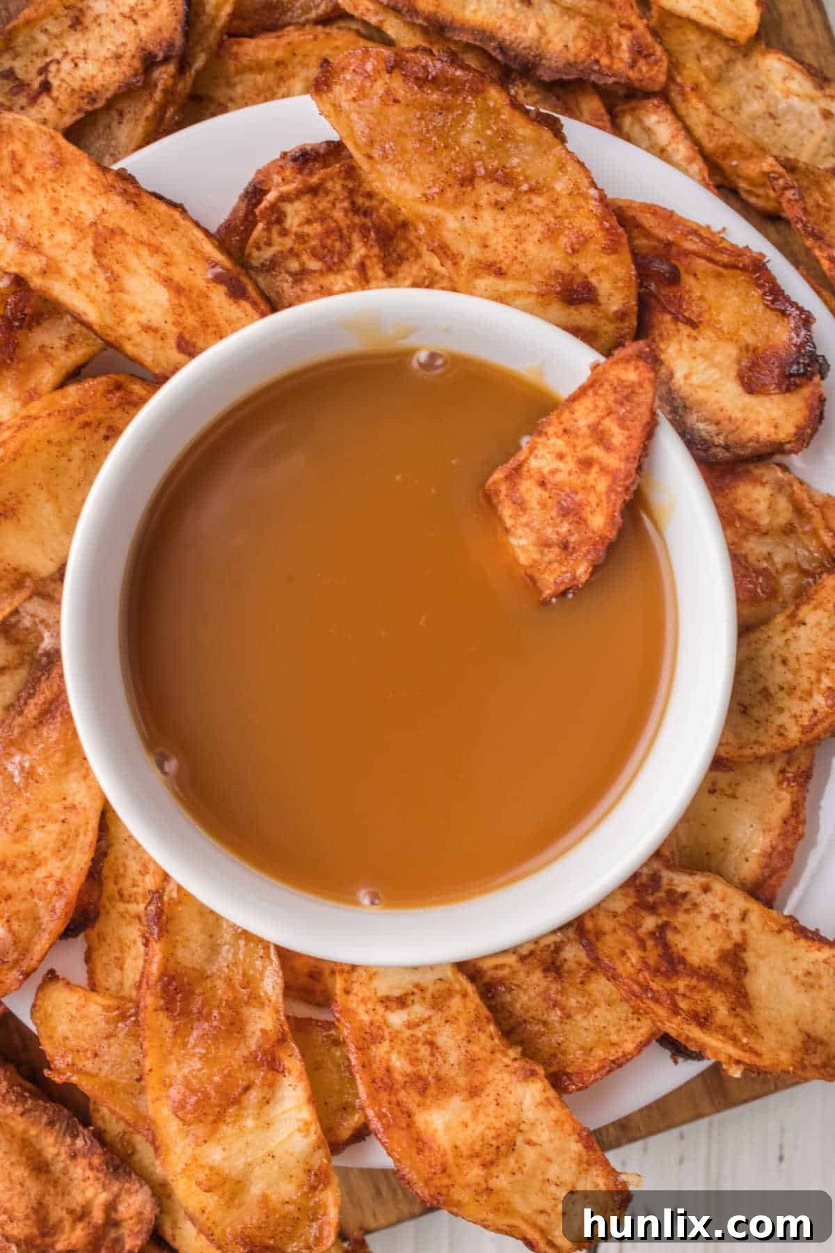 A bowl of caramel dip surrounded by air-fried apple slices, ready for dipping.