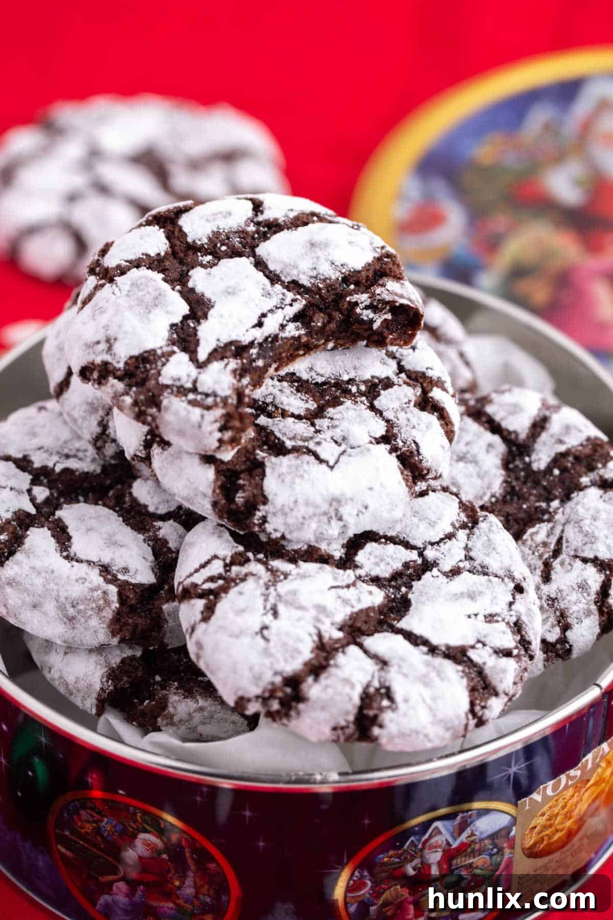 A generous pile of chocolate crinkle cookies, perfectly crinkled and dusted with powdered sugar, arranged invitingly in a holiday tin, showcasing their delightful texture and festive appeal.