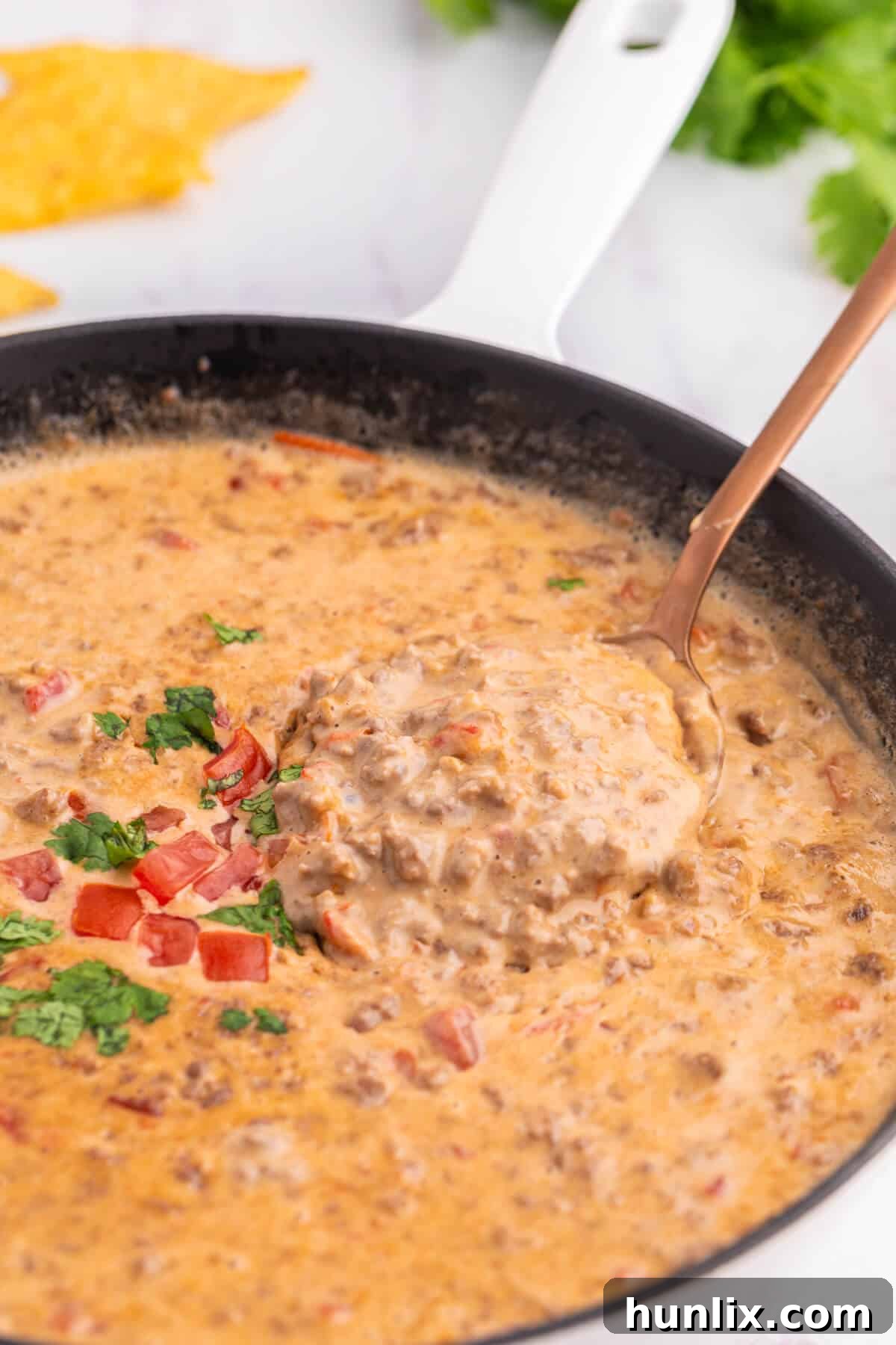A spoon in a skillet filled with Rotel Dip, garnished with cilantro.