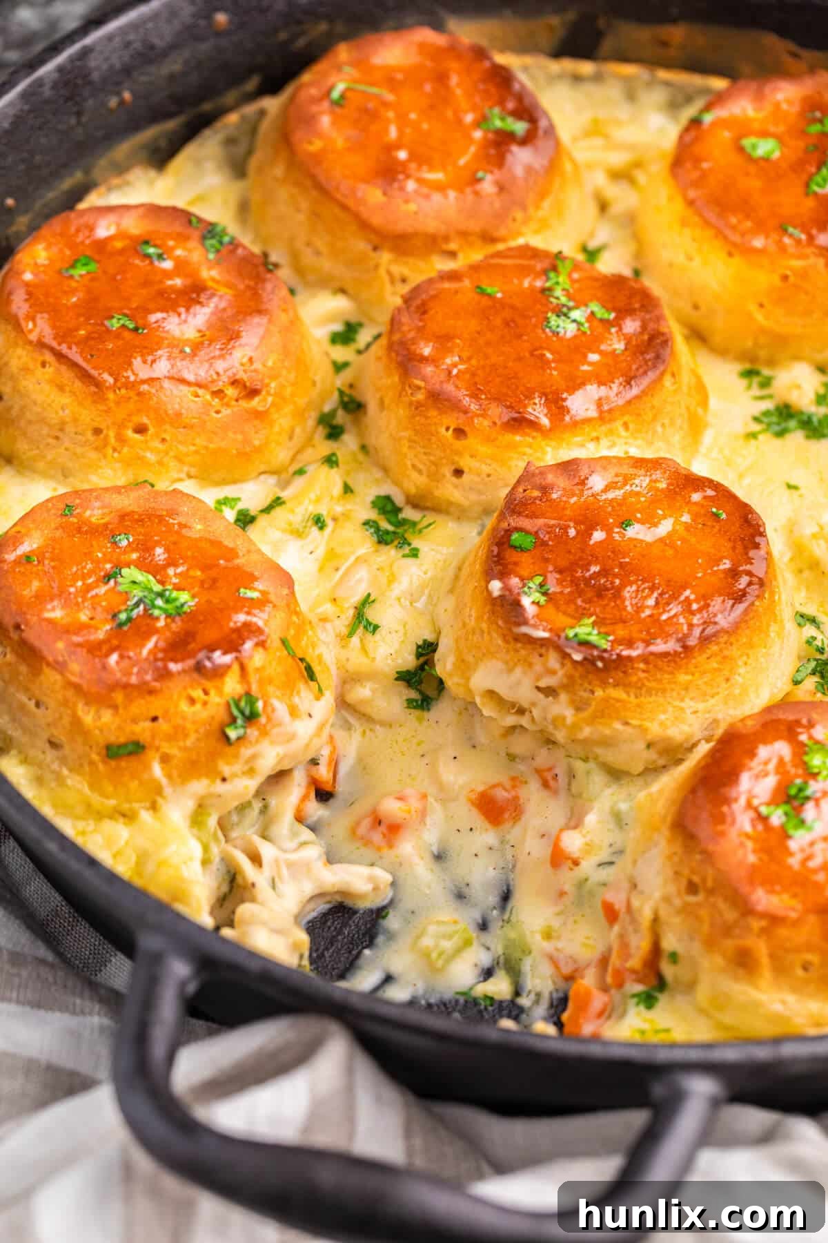 A serving spoon lifting a piece of cast iron skillet chicken pot pie from the pan, showing the creamy filling and golden biscuit.