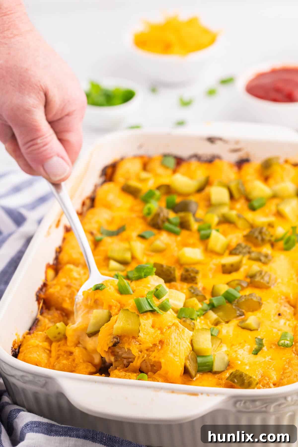 A hand holding a serving spoon with cheeseburger tater tot casserole.