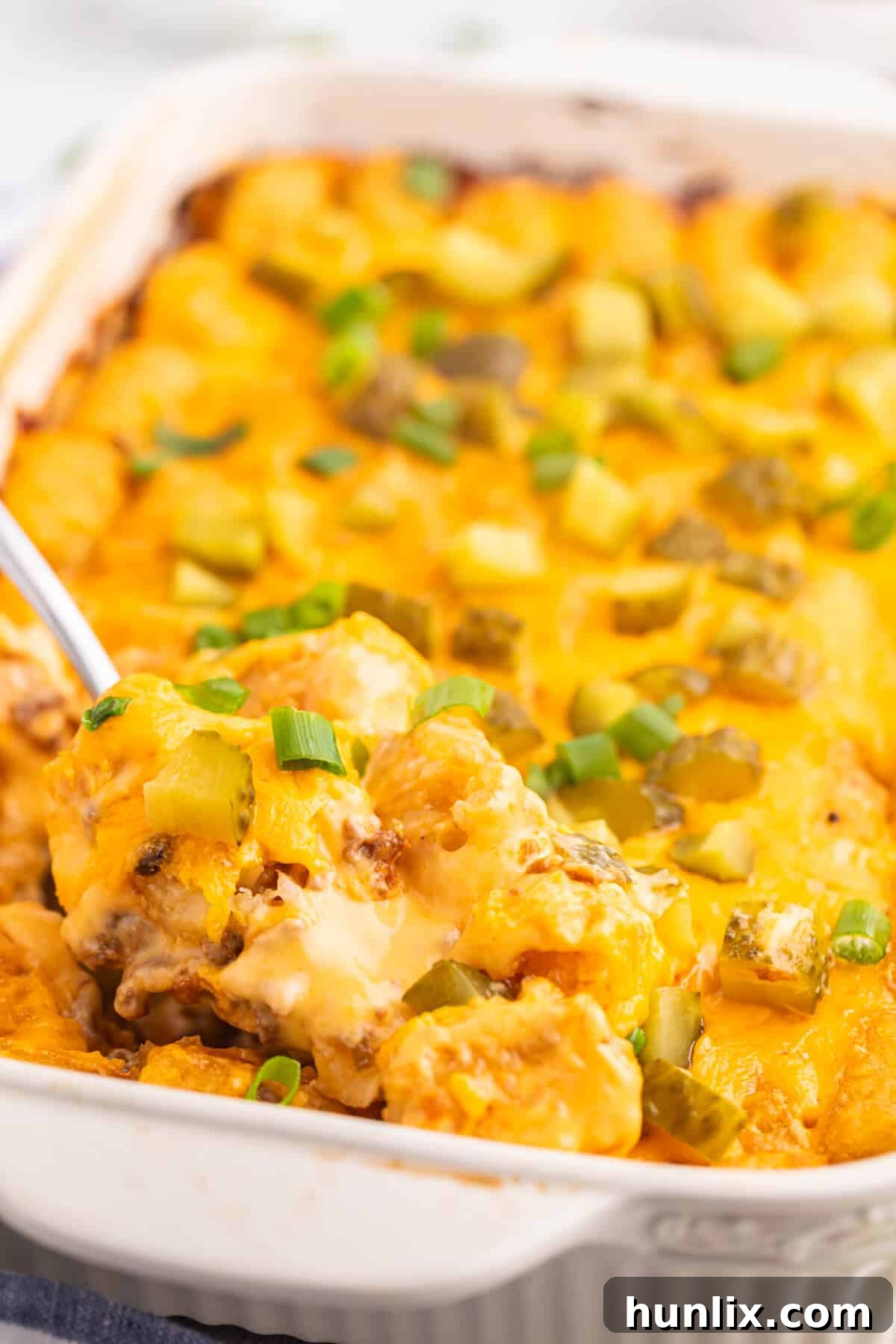 A serving spoon in a pan of cheeseburger tater tot casserole.