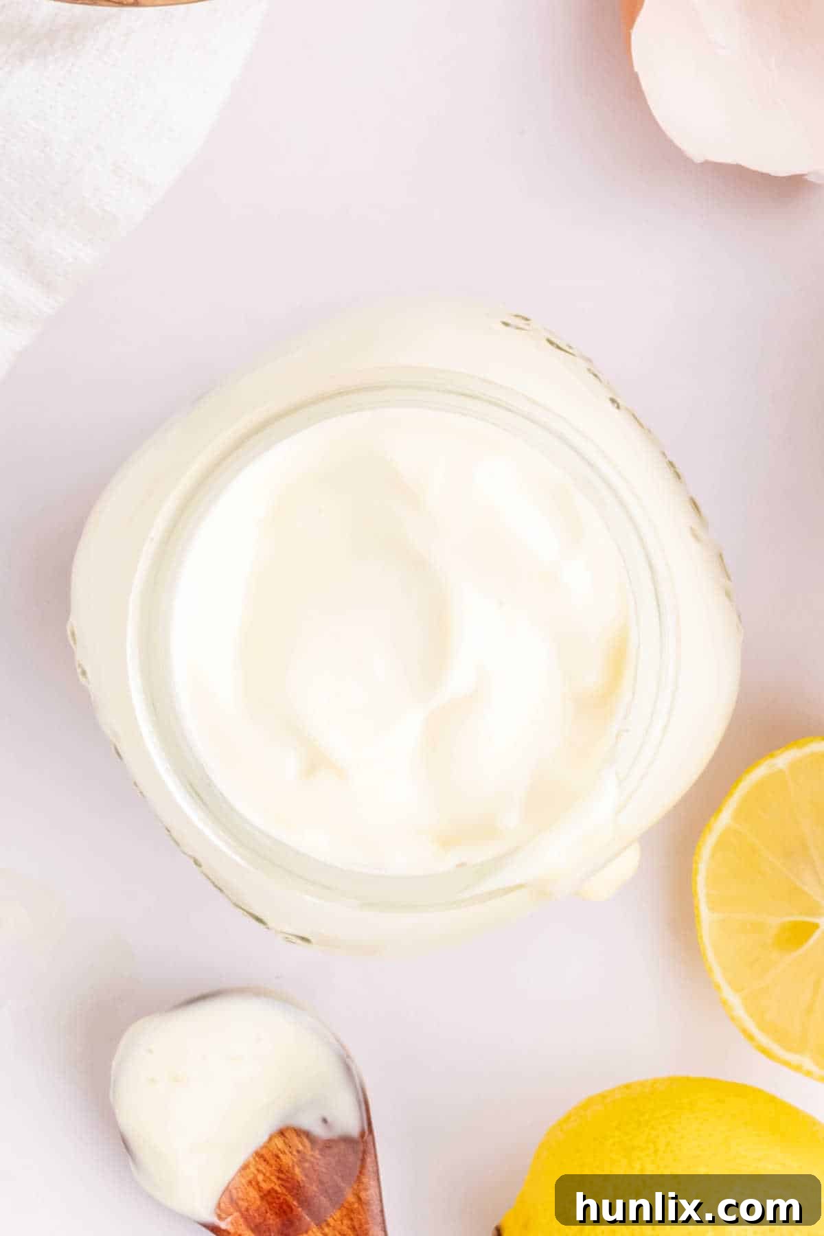 A jar of mayonnaise and a wooden spoon covered in mayonnaise, highlighting its smooth texture and rich color.