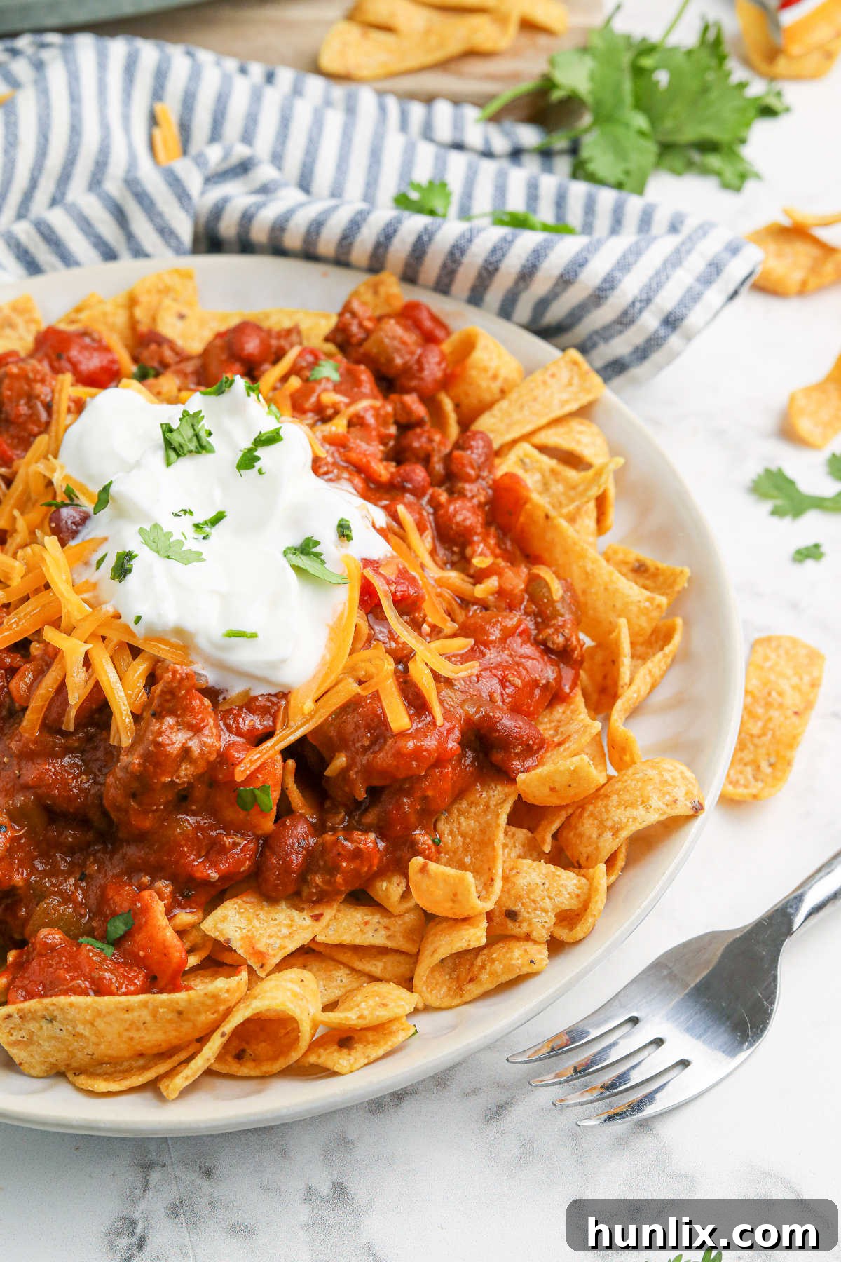 A close-up of a Frito Chili Pie serving, showcasing melted cheese and fresh toppings.