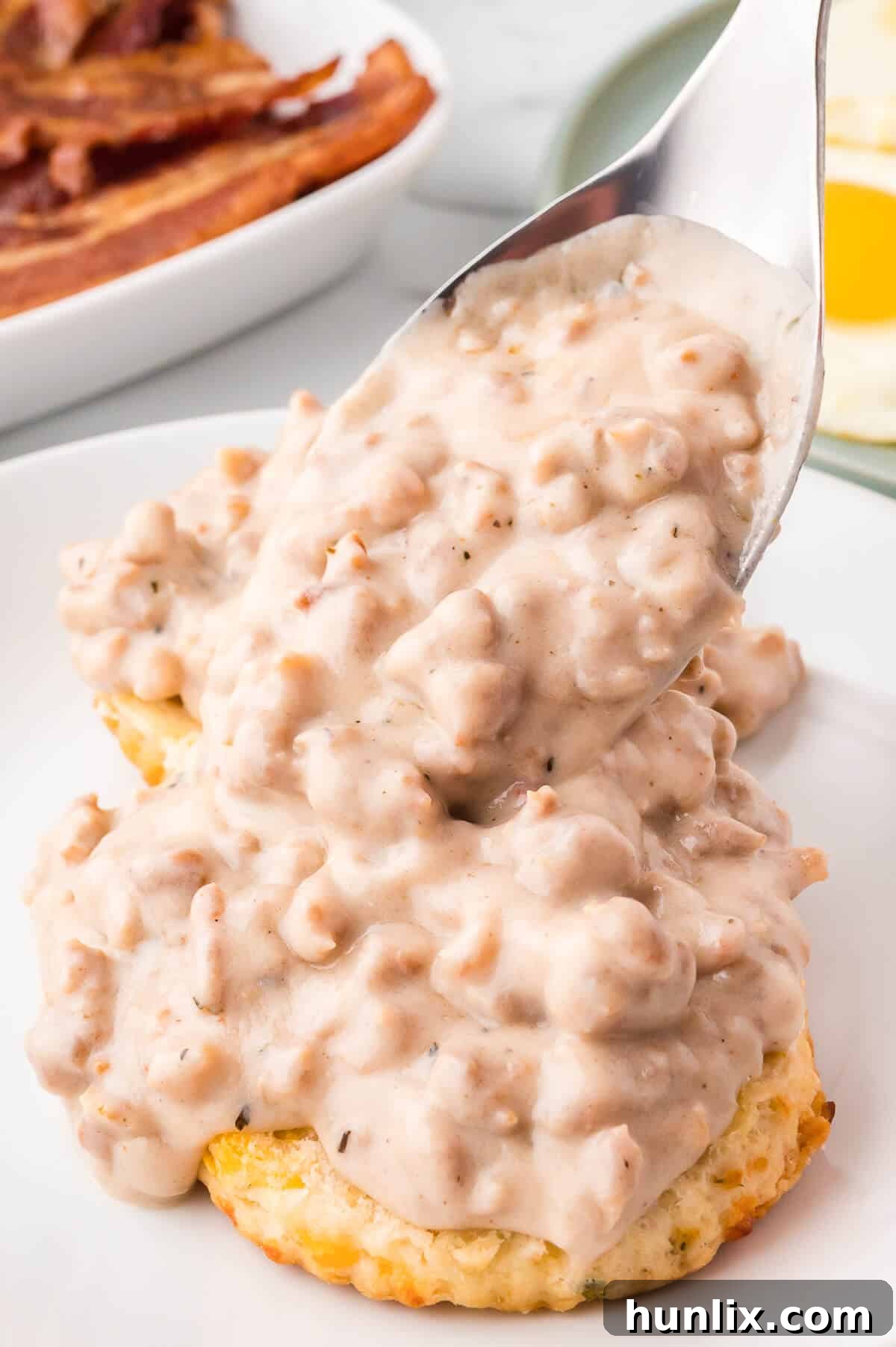 A serving spoon pouring sausage gravy over biscuits.