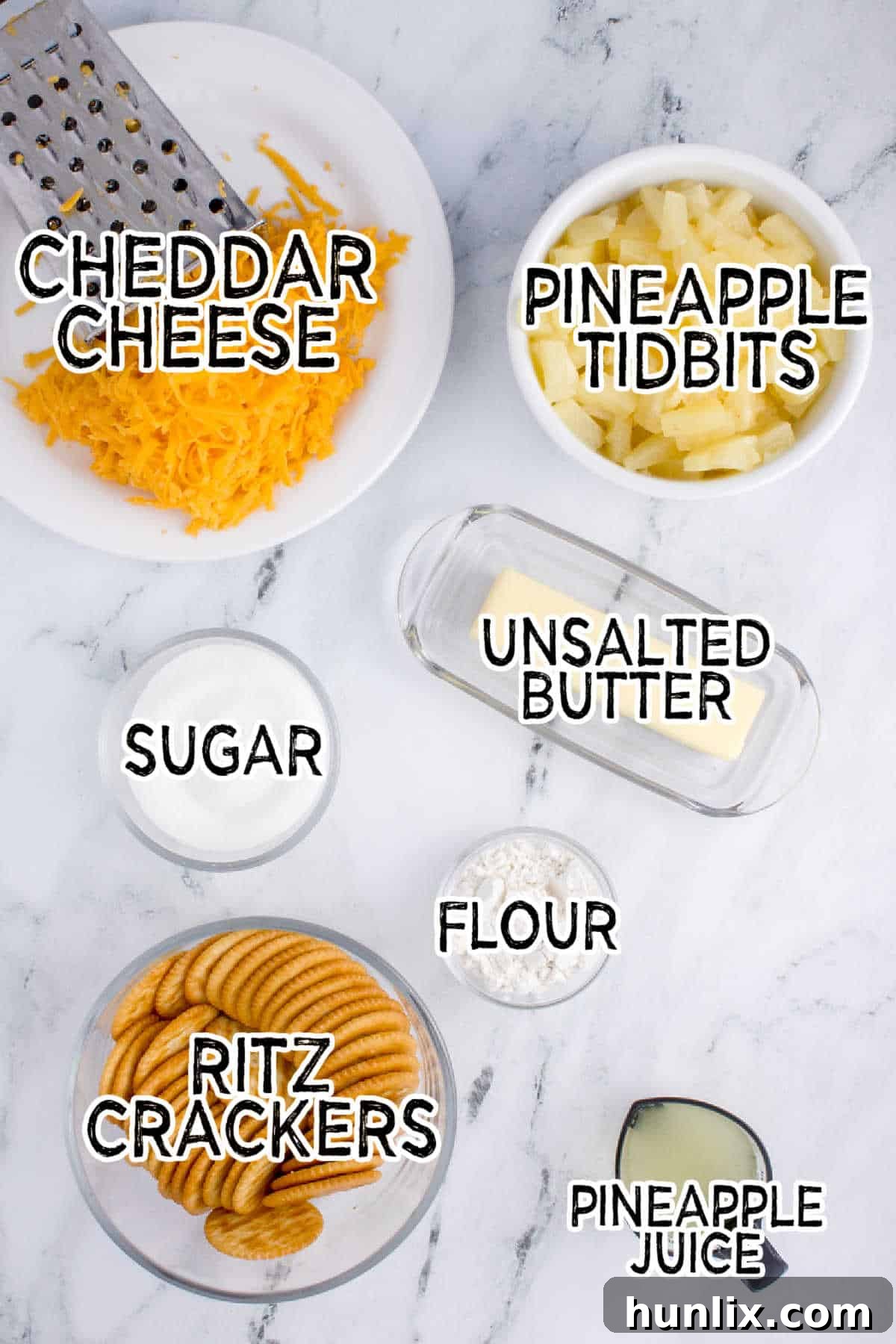 Ingredients for pineapple casserole arranged on a kitchen counter: canned pineapple tidbits, sugar, melted butter, flour, grated sharp cheddar cheese, crushed Ritz crackers, and a small bowl of pineapple juice.